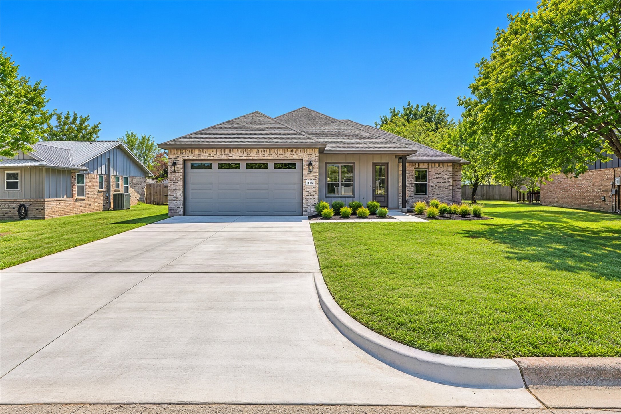 Single-story brick-and-gray house with a two-car garage, broad driveway, and landscaped lawn.