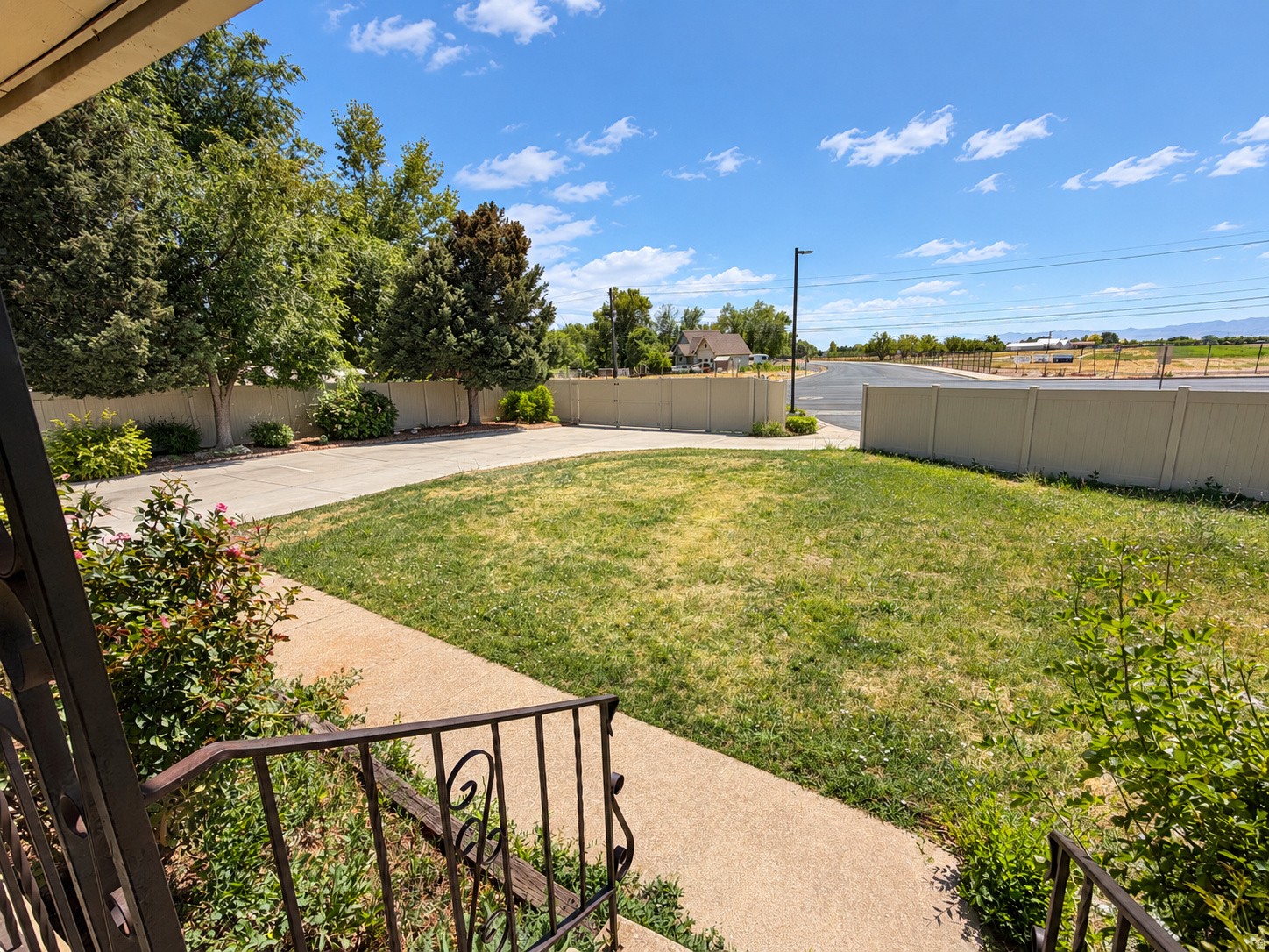 Front yard with a lawn, paved walkway, mature trees, and gated driveway entrance.