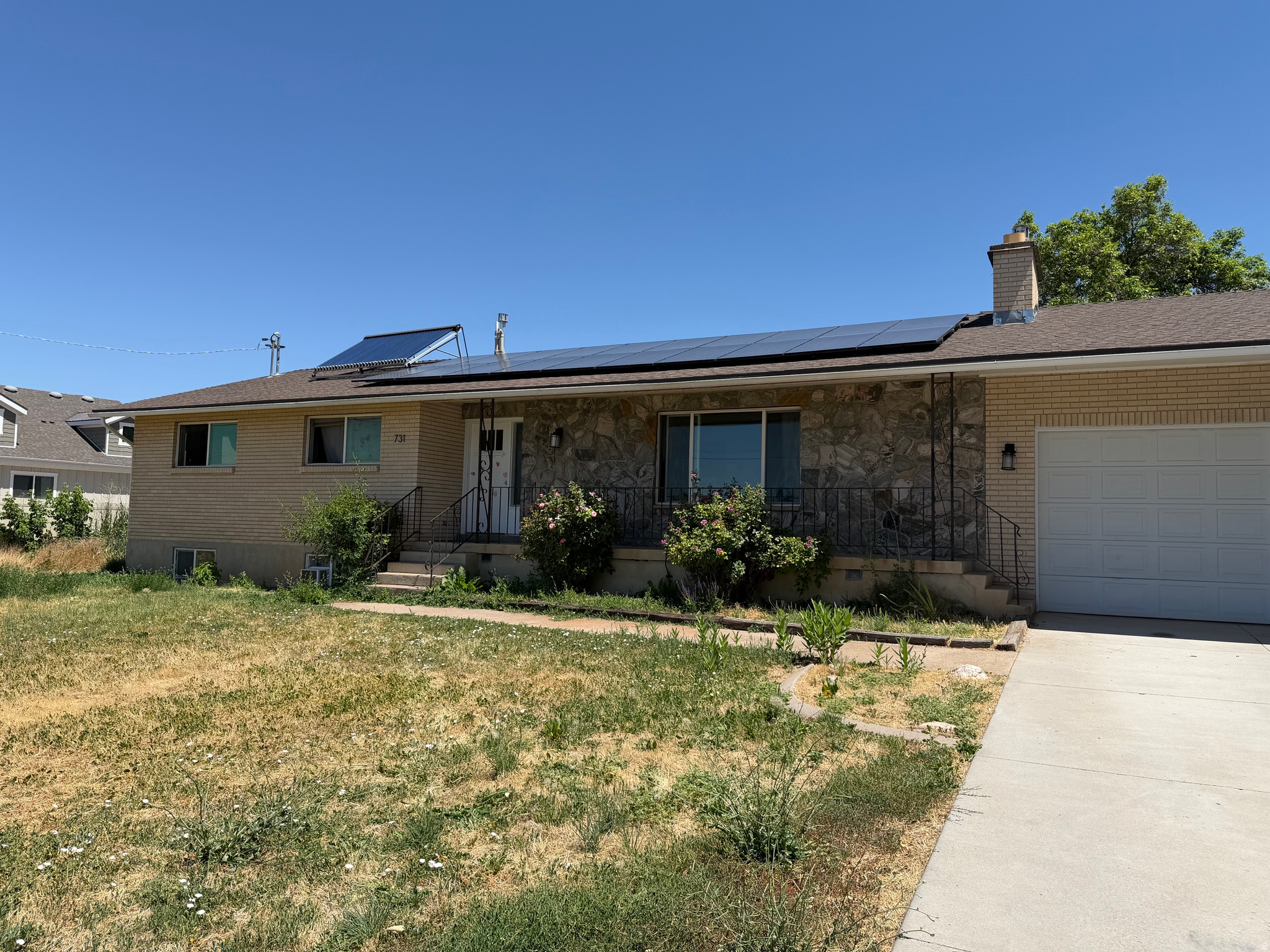 Single-story brick-and-stone house with rooftop solar panels, a covered porch, and an attached garage.