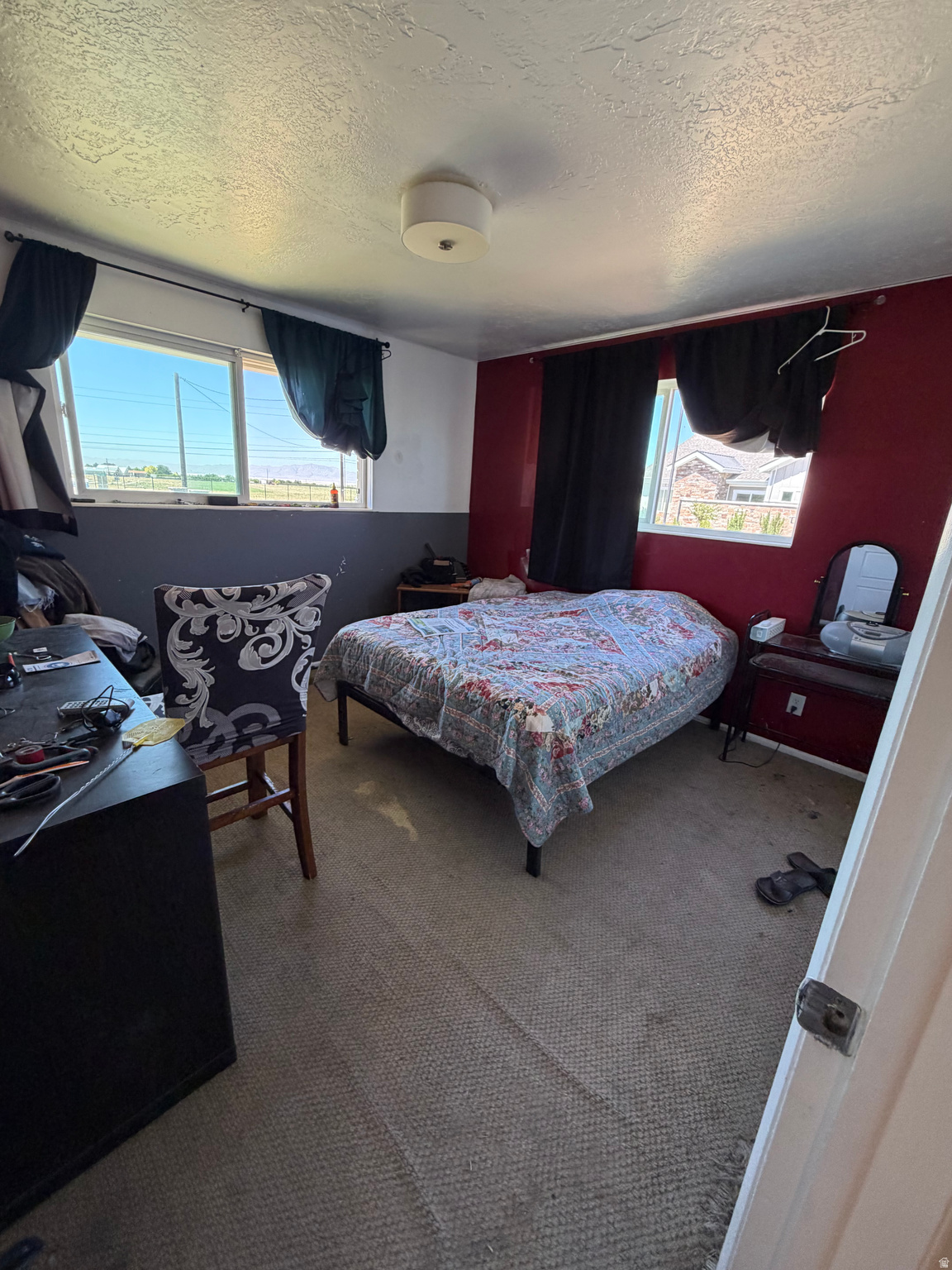 Bedroom with a patchwork-covered bed, red accent wall, and two windows with dark curtains.