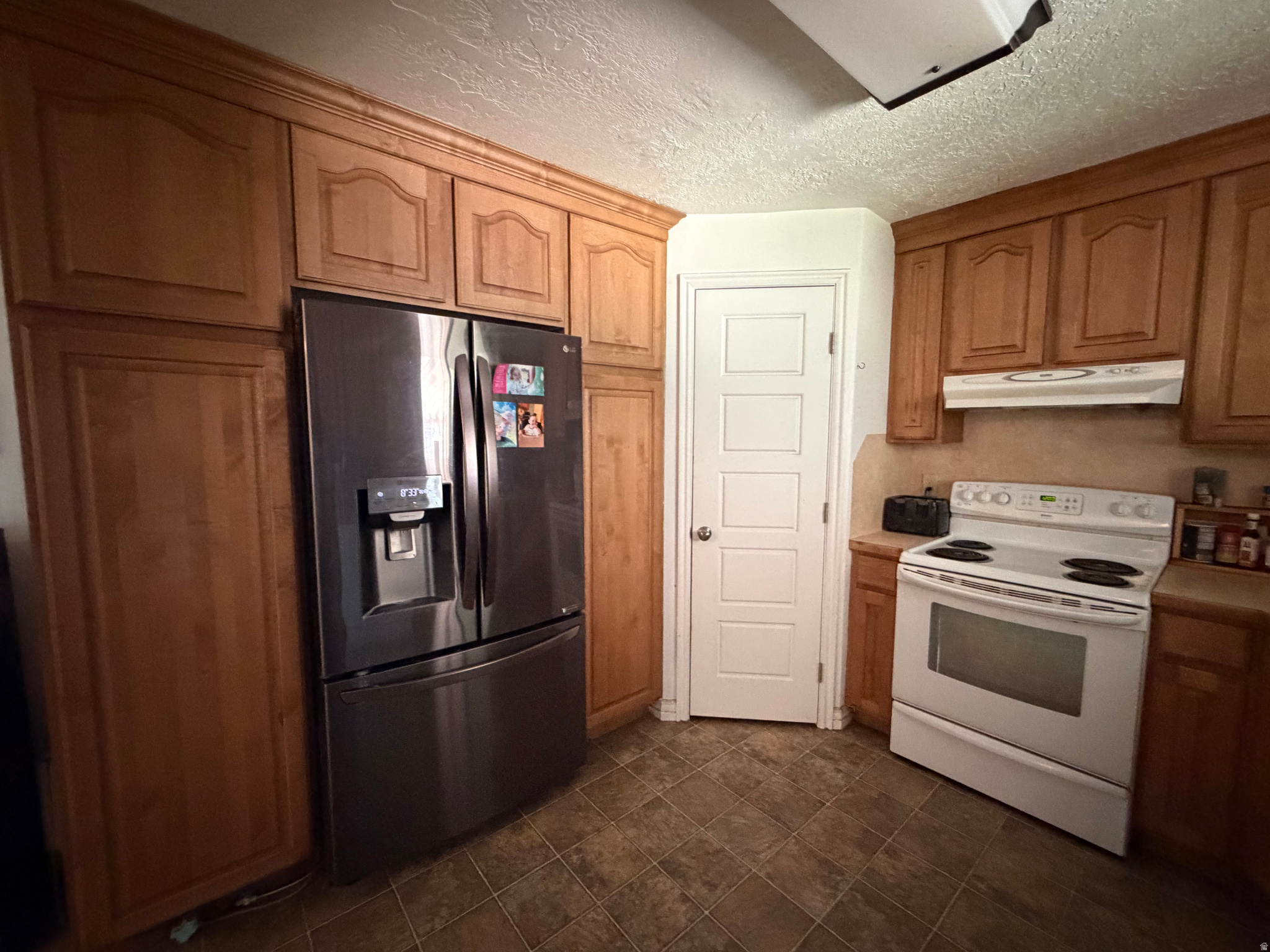 Kitchen with wood cabinetry, dark refrigerator, white electric range, and tiled floor.