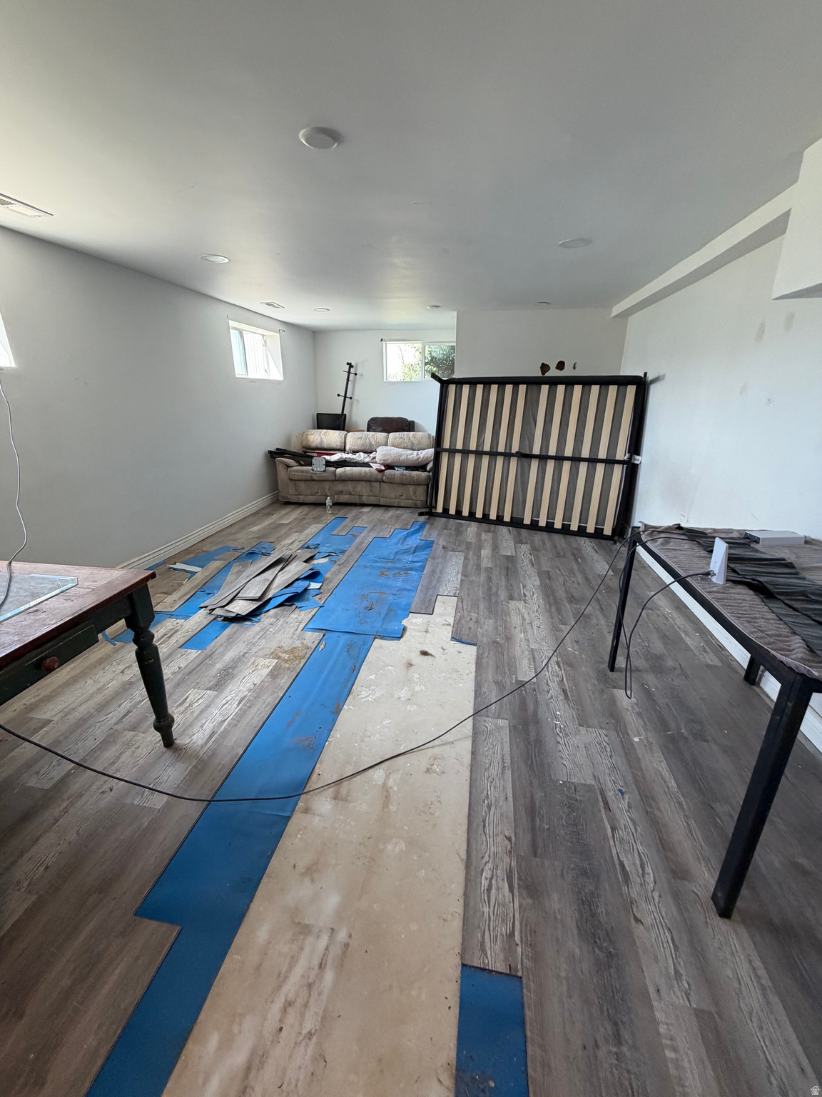 Interior room with flooring removed, blue underlayment, exposed subfloor, sofa, and upright bed frame.
