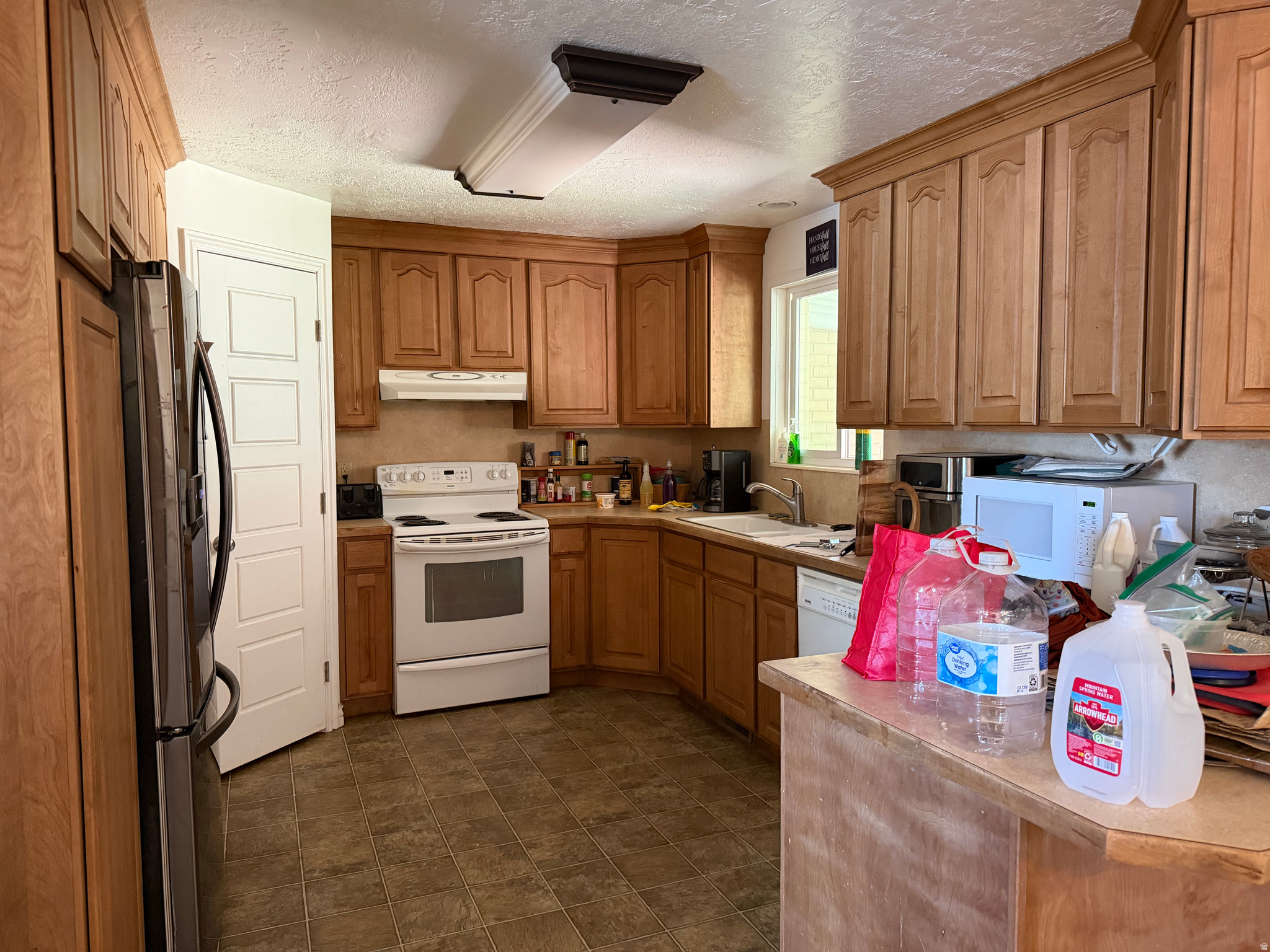 Kitchen with extensive wood cabinetry, brown tile floors, and a cluttered island.