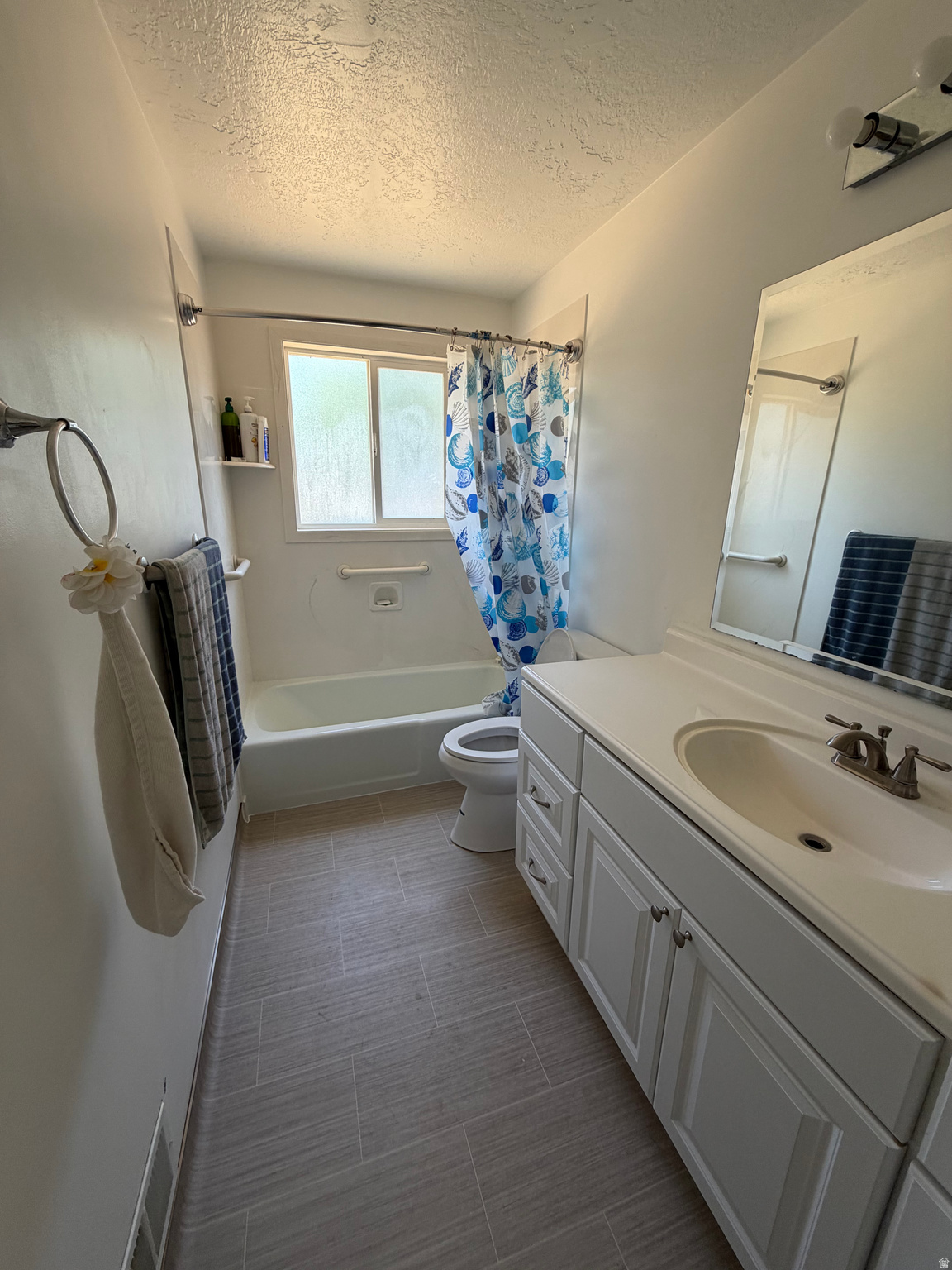 Bathroom with a white vanity, bathtub, frosted window, and blue patterned shower curtain.