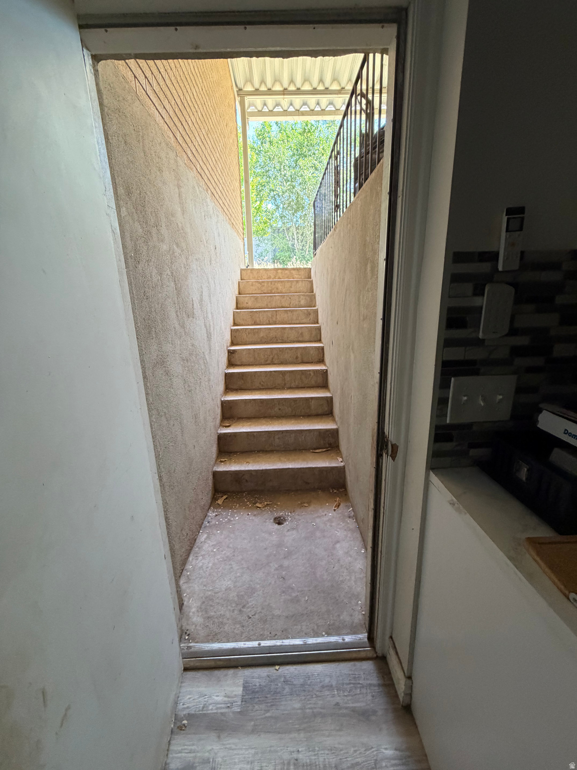 Concrete stairs rise to a covered landing with a metal railing and leafy trees beyond.