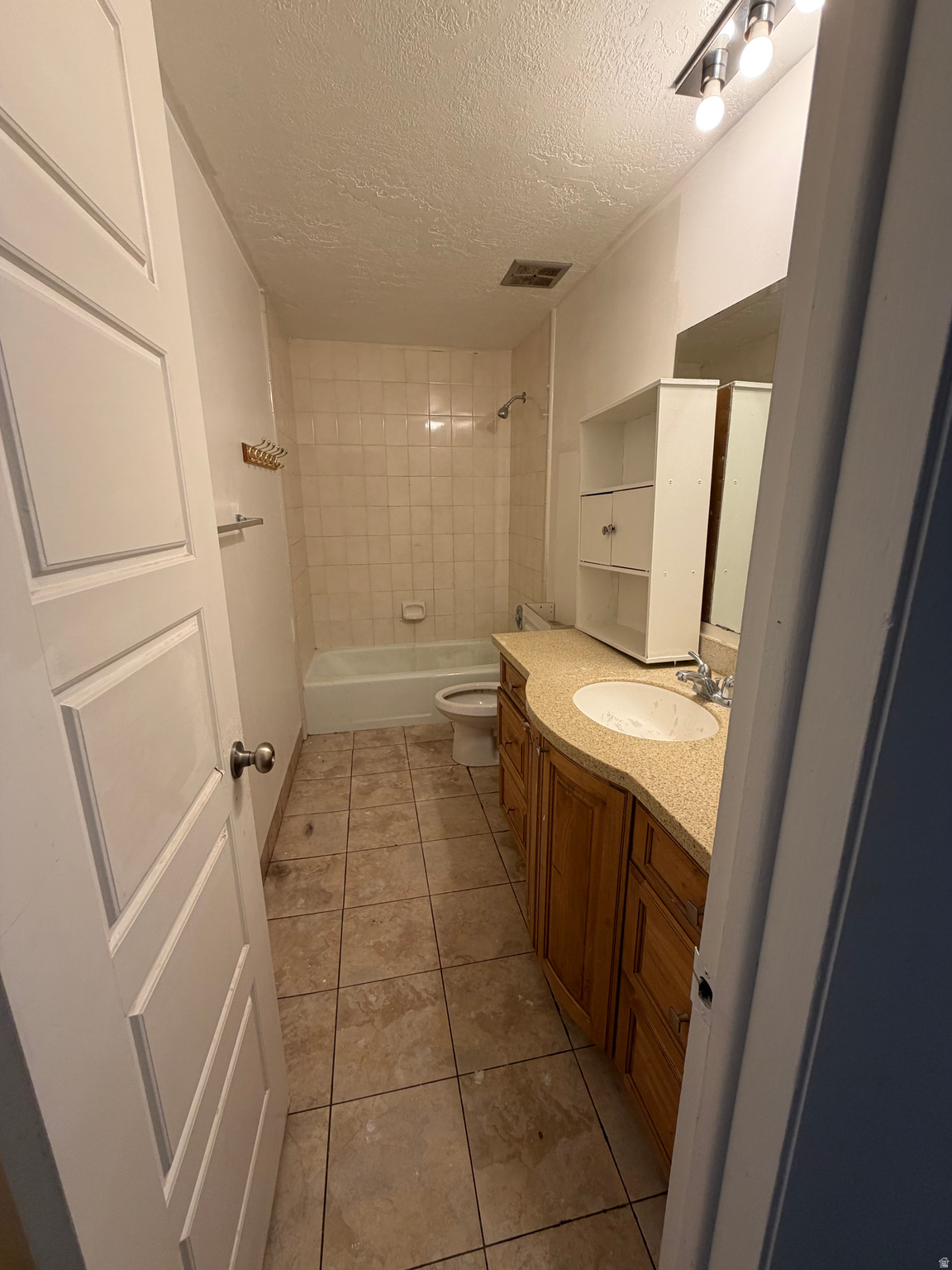 Bathroom with tiled tub and shower, toilet, and wood vanity with a single sink.