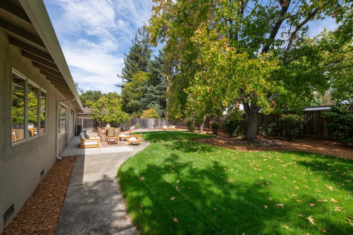 Backyard lawn and mature shade trees beside a patio with outdoor seating.