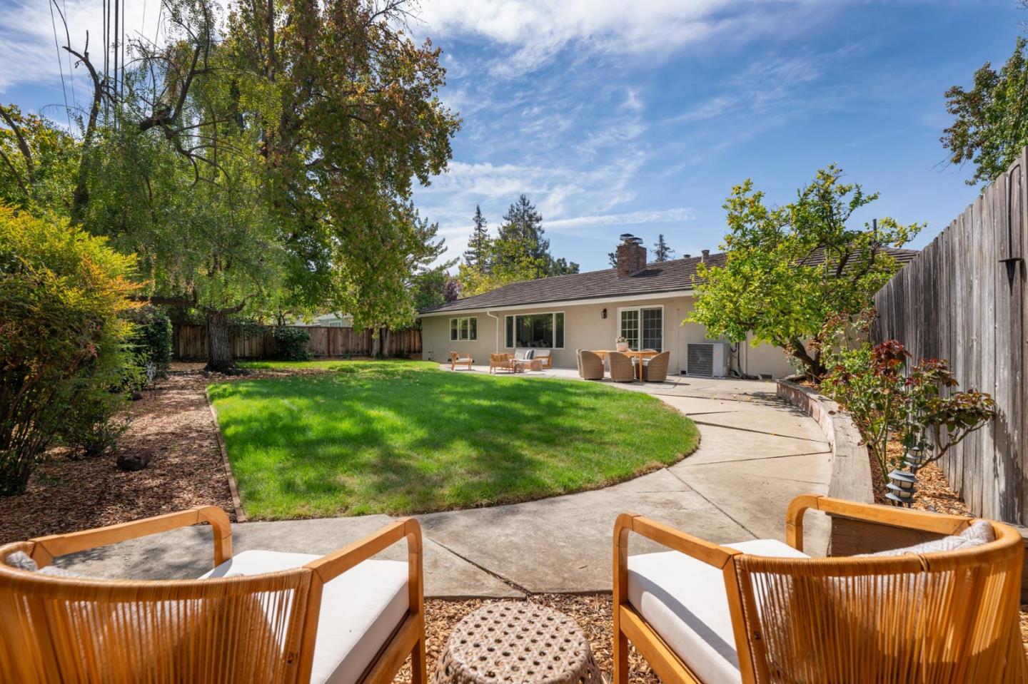 Backyard with a curved patio, green lawn, outdoor seating, and mature trees.