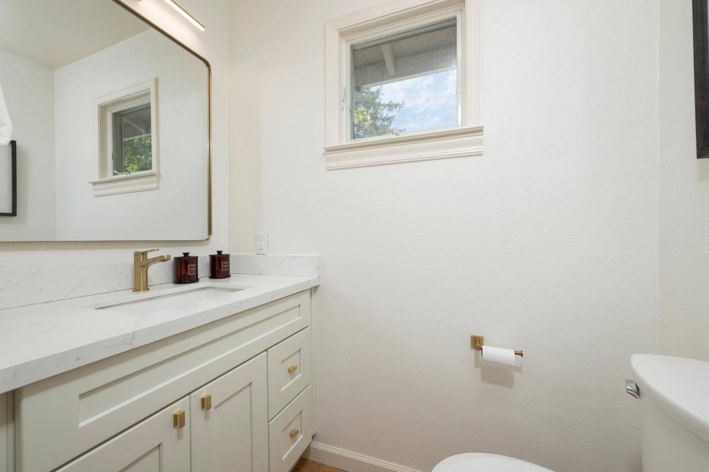Bathroom with a white vanity, veined countertop, brass faucet, and window above the sink.