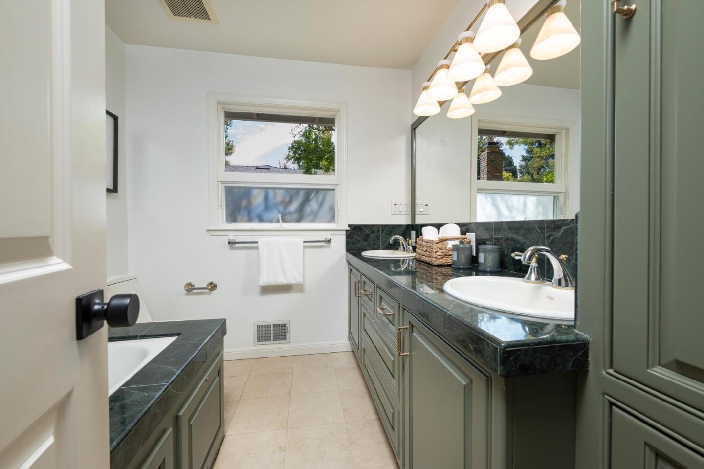 Bathroom with a double vanity, dark stone counters, gray-green cabinets, and a large mirror.