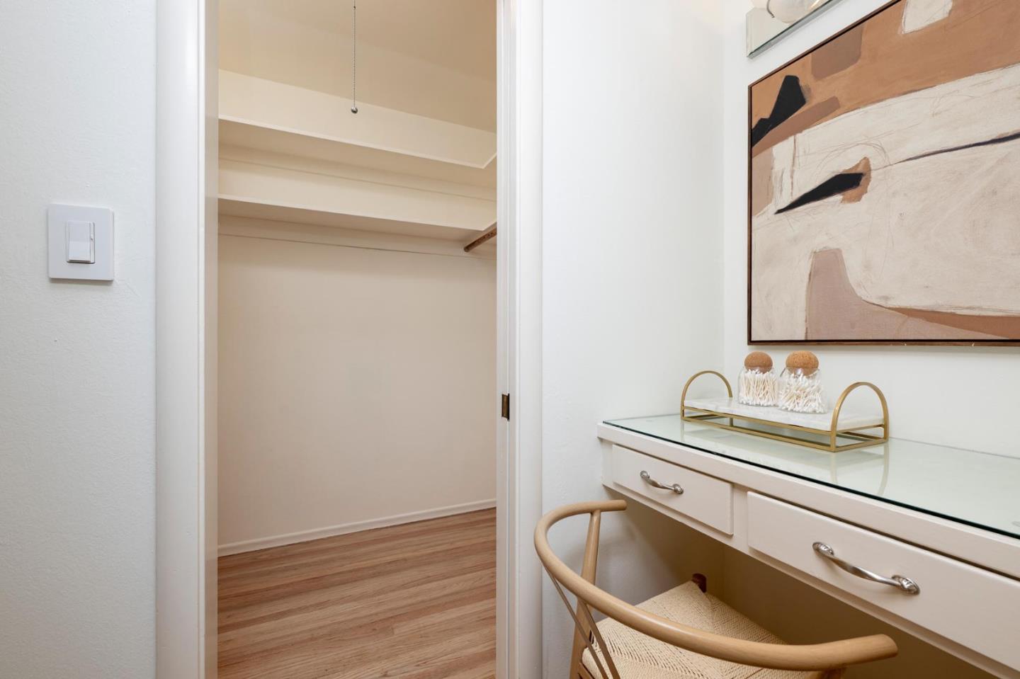 Dressing area with an open walk-in closet and a white vanity with a woven chair.