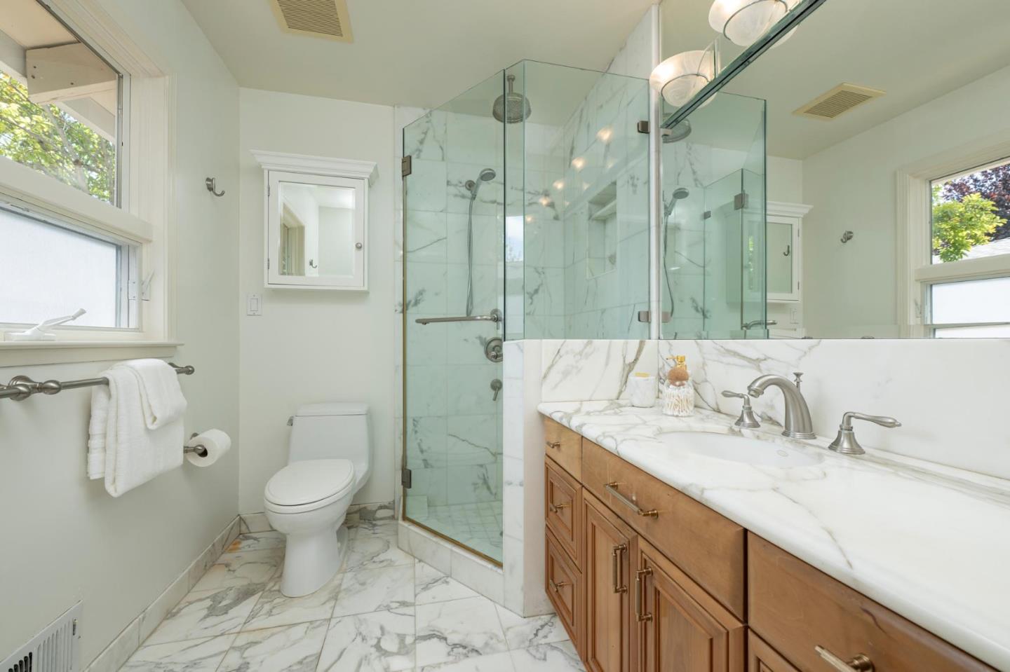 Bathroom with a glass-enclosed marble shower and marble vanity above wood cabinets.