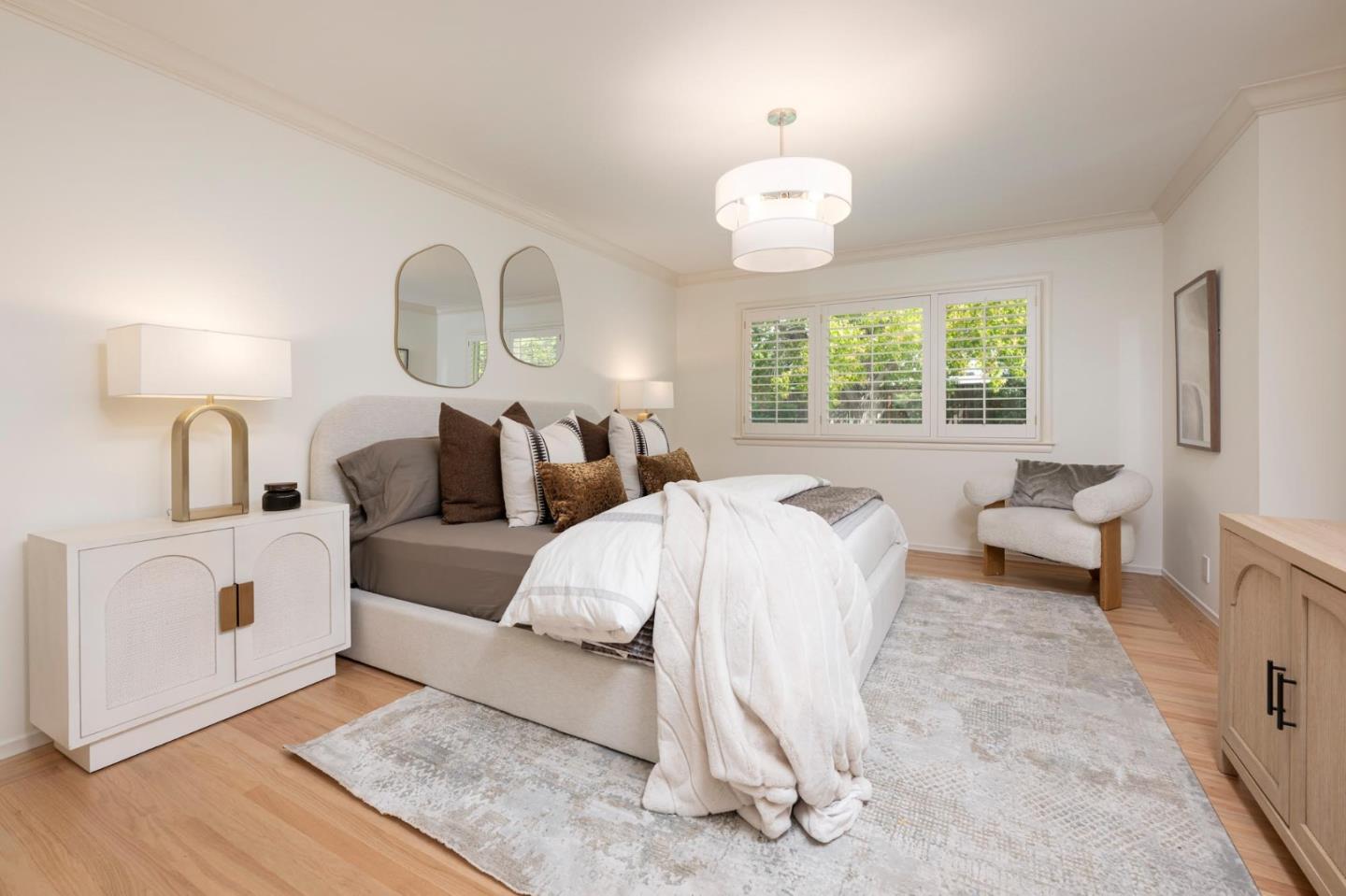 Staged bedroom with a white-and-taupe bed, patterned rug, and shuttered window.