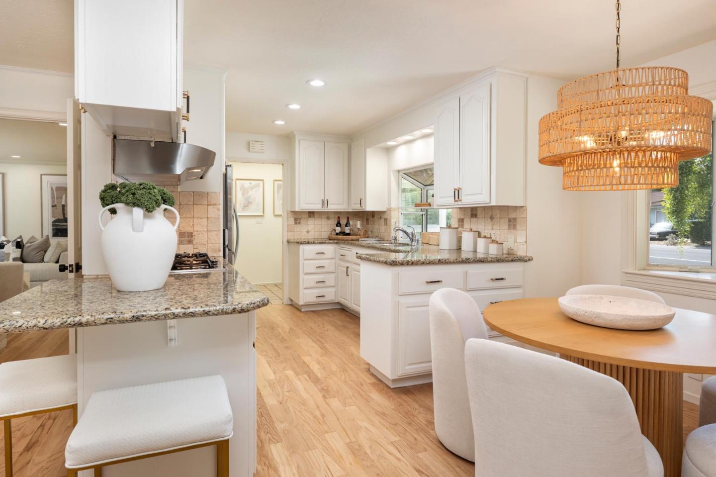 Kitchen and dining area with white cabinetry, granite island, wood floors, and a round table beneath a woven pendant.