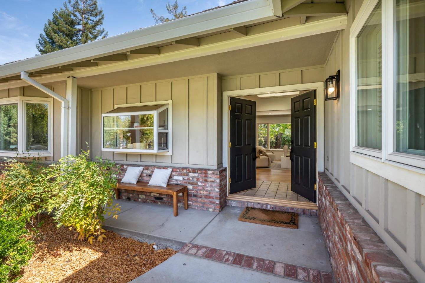 Covered front porch with open black double doors, a brick planter wall, and a cushioned bench.