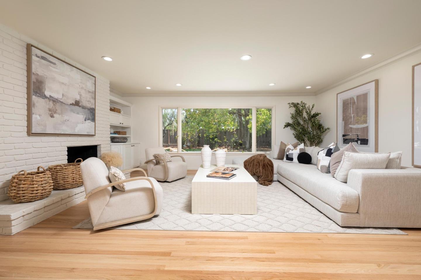 Staged living room with a white brick fireplace and large windows overlooking a leafy garden.