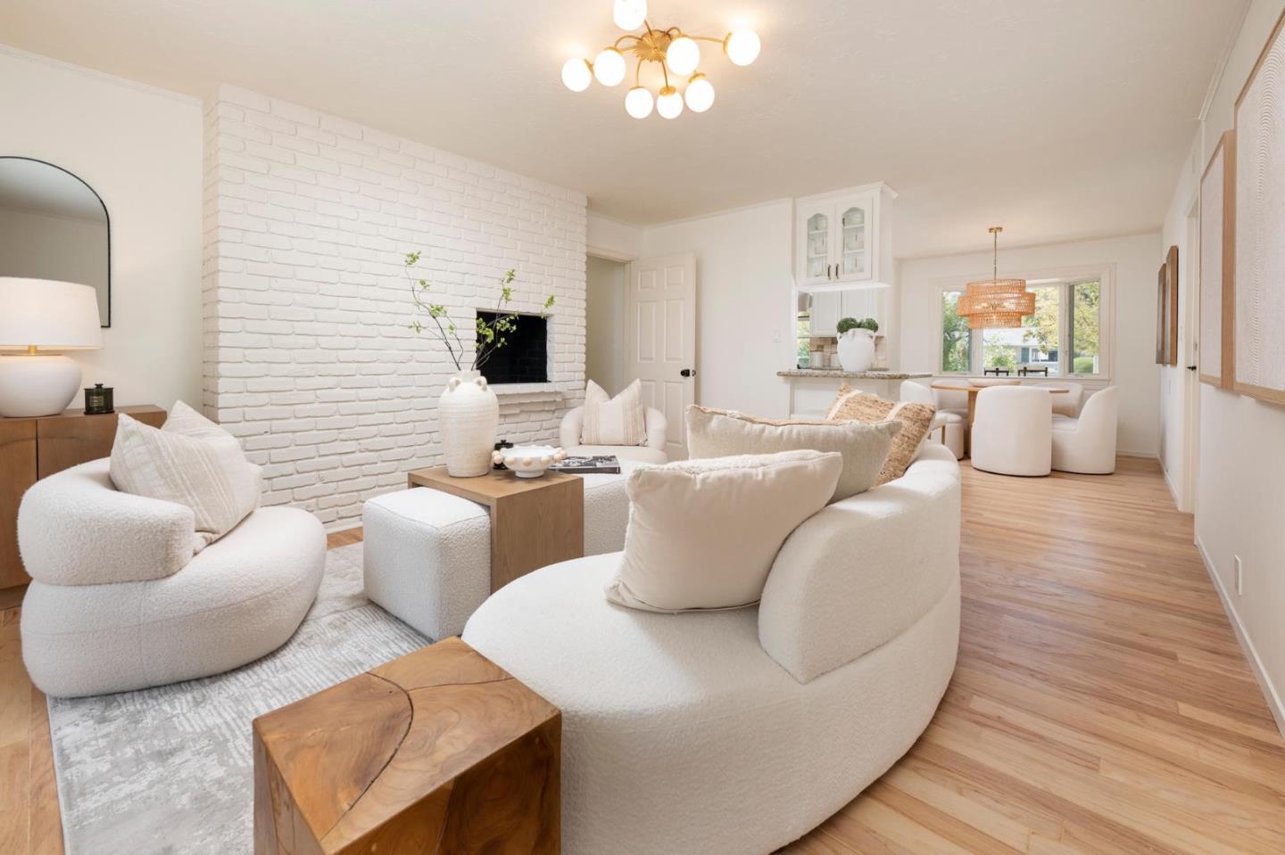 Living room with curved white sofas, a white brick fireplace, and an open dining area.
