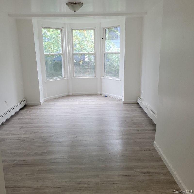 Vacant room with gray plank flooring, baseboard heaters, and three tall bay windows.