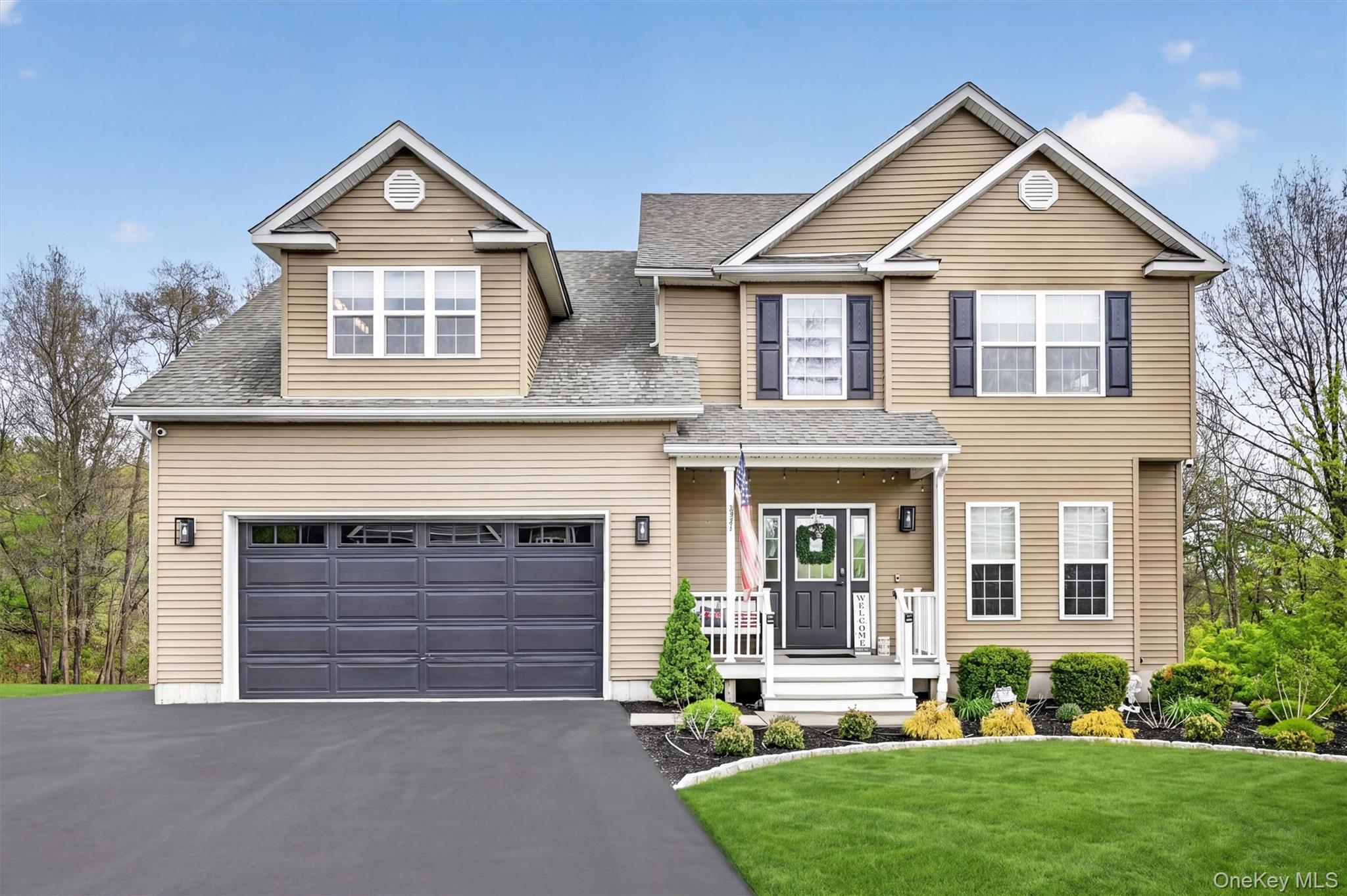 Two-story beige home with a dark double garage, covered porch, landscaped garden, and broad driveway.