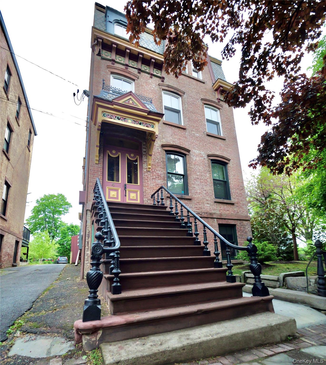 Brick townhouse with an ornate entrance canopy and broad raised stoop with black railings.