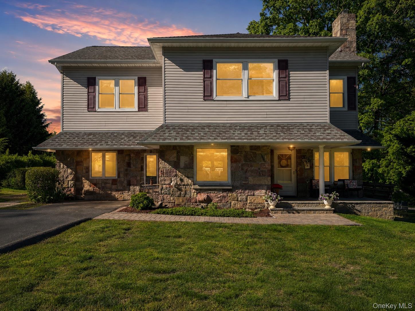 Two-story home with a stone lower facade and glowing windows beneath a pink dusk sky.