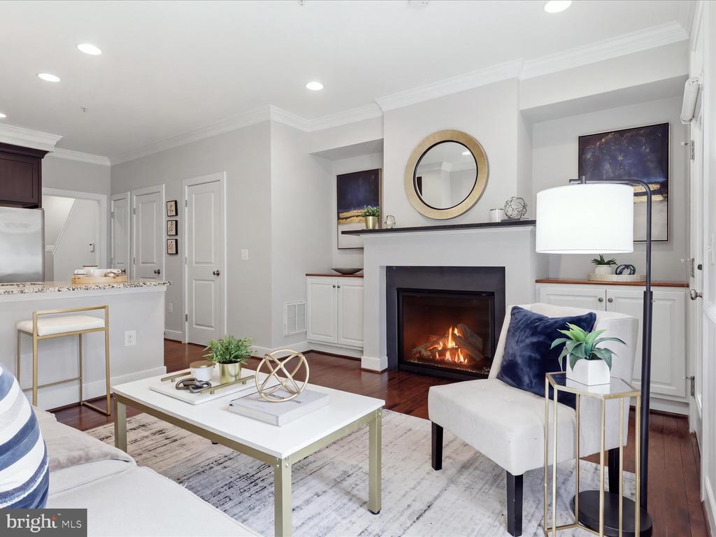 Staged living room with a lit fireplace, white seating, and an open kitchen.