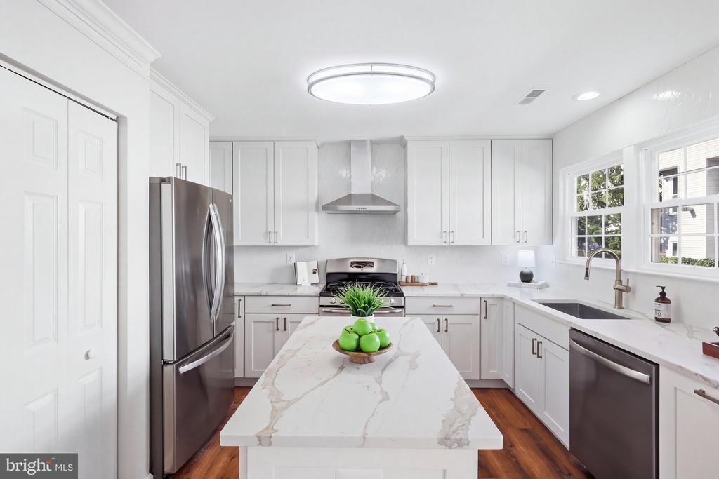 Bright white kitchen with a marble island, stainless steel appliances, and windows above the sink.