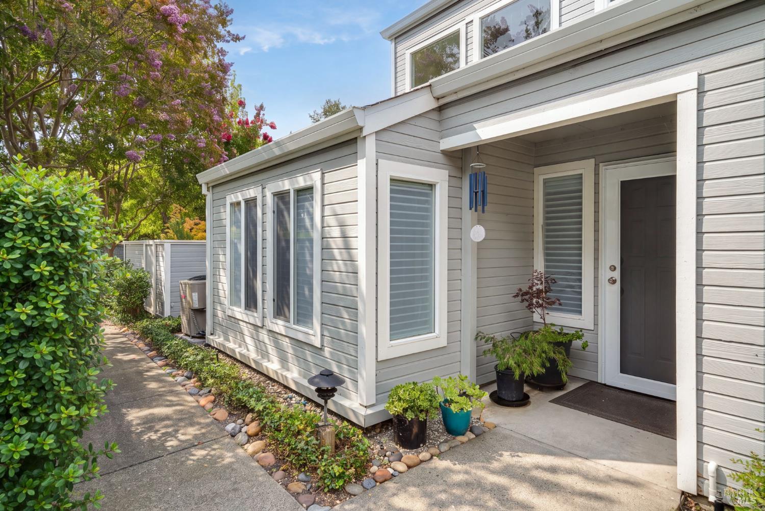 Light gray home with a covered entry and landscaped walkway beneath flowering trees.