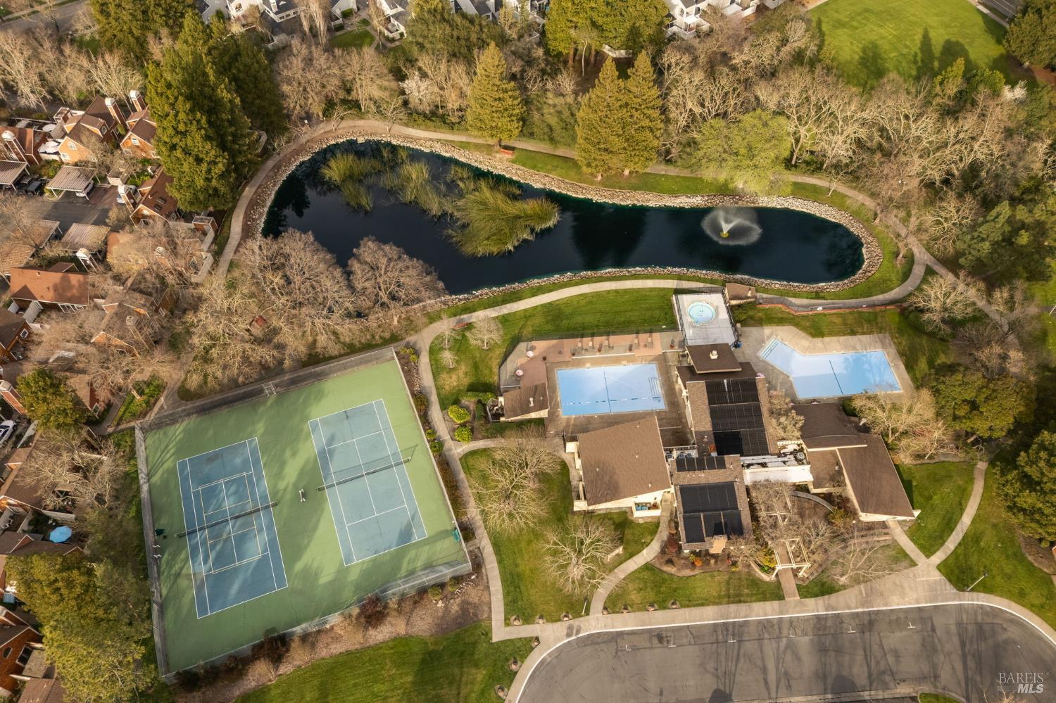 Aerial view of a community pond with a fountain, tennis courts, and swimming pools.