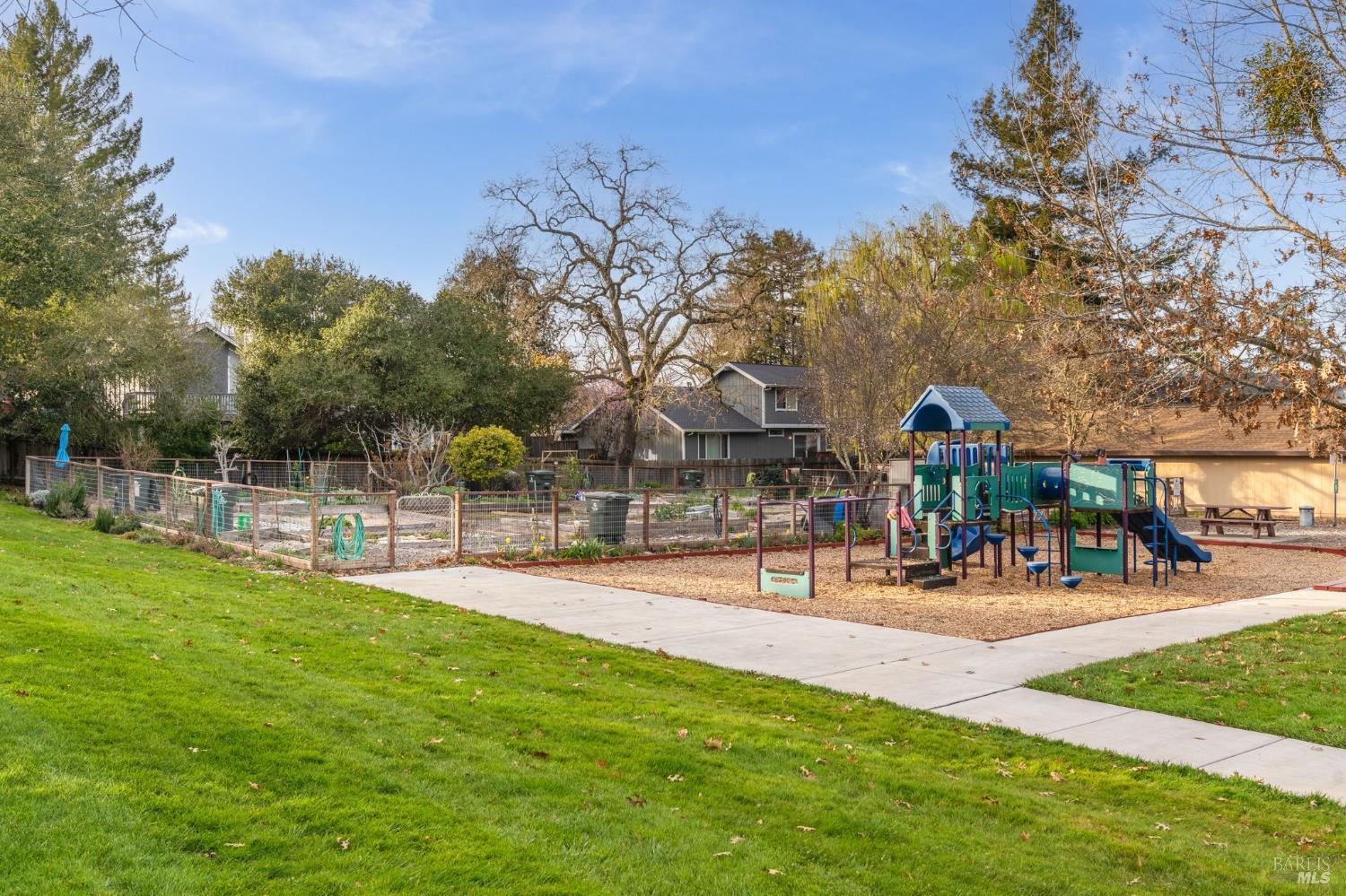 Community playground beside a fenced garden, with a paved path and grassy lawn.