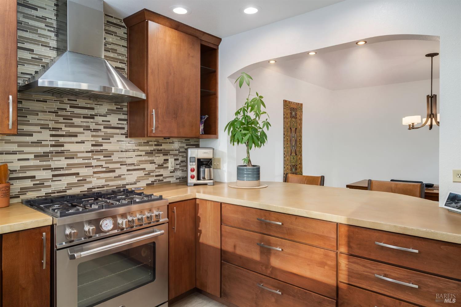 Kitchen with warm wood cabinetry, a stainless steel range, and a mosaic tile backsplash.