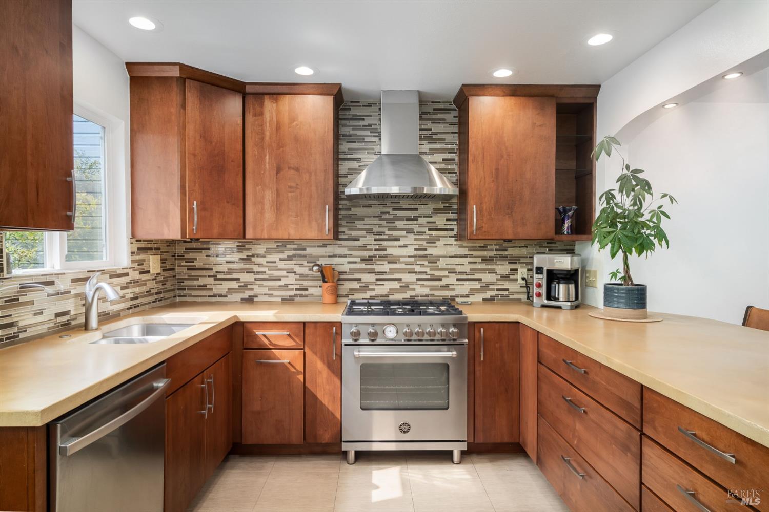 Kitchen with reddish-brown cabinetry, mosaic tile backsplash, and stainless-steel range.