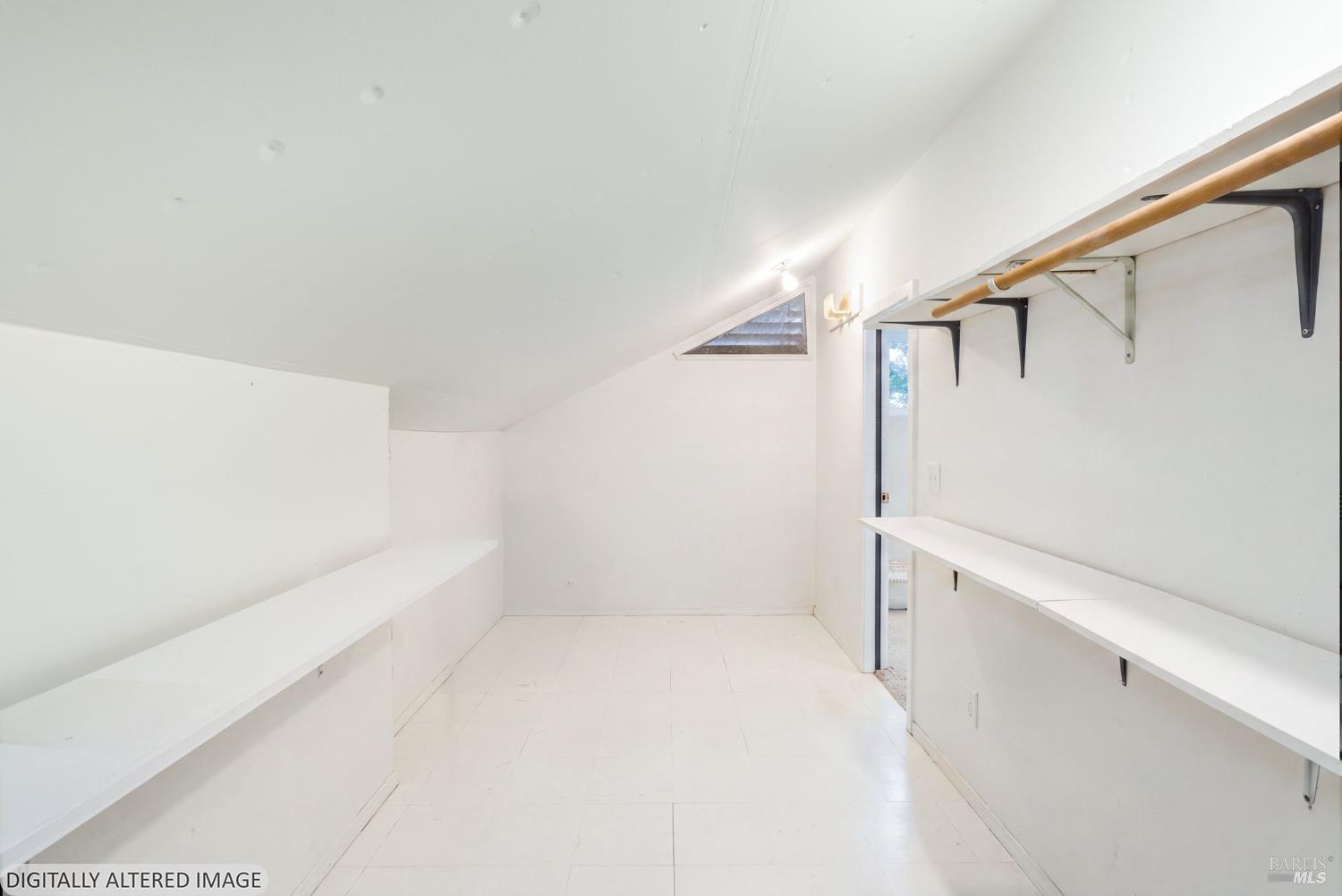 Empty closet with built-in shelves, a wooden hanging rod, and a sloped ceiling.