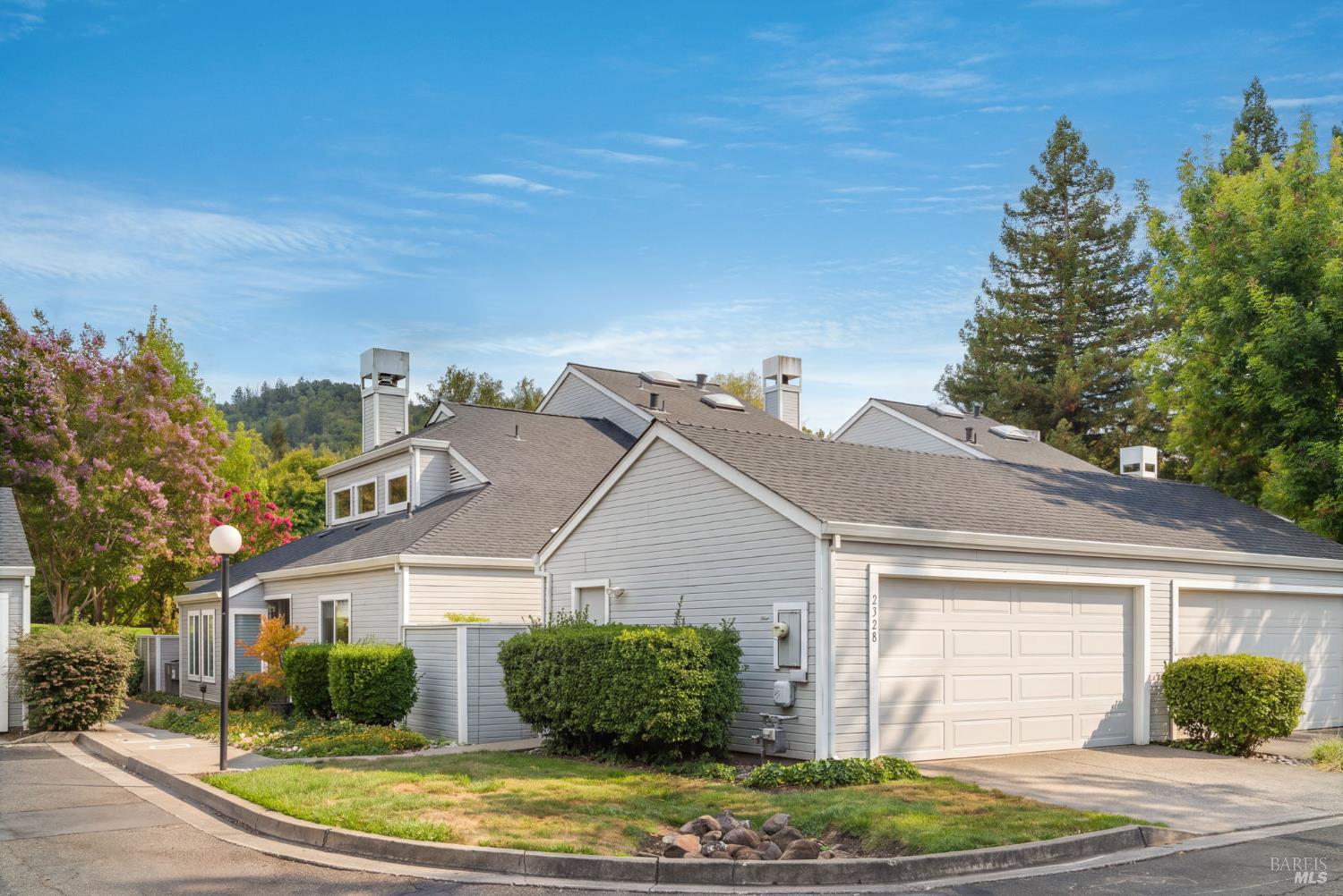 Gray-sided home with an attached double garage, gabled roofs, and flowering trees.