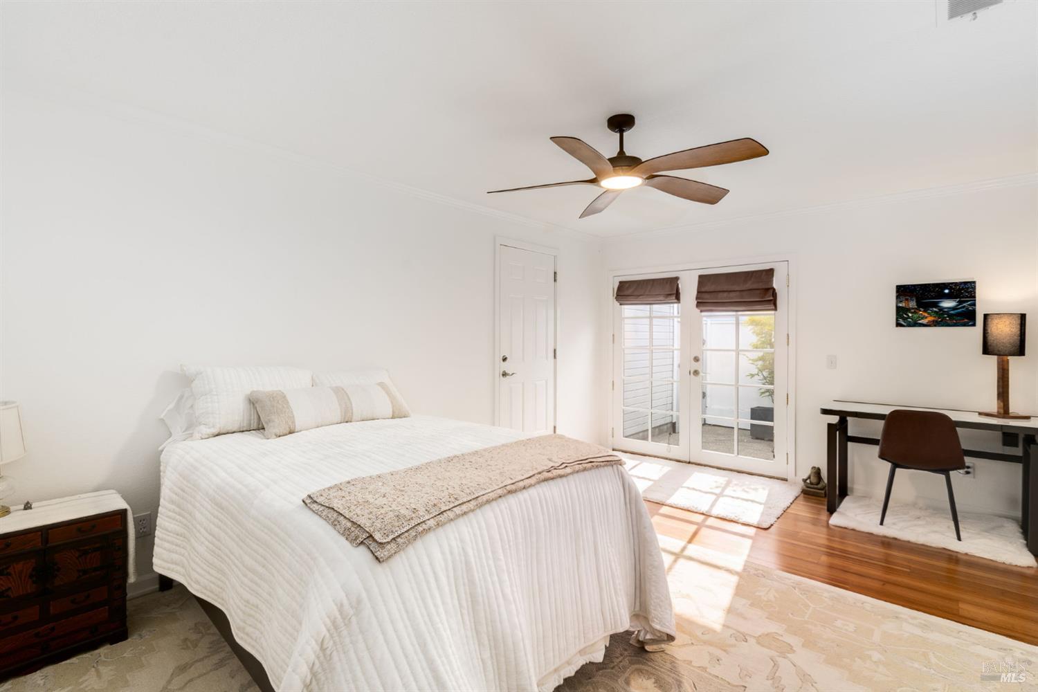 Bright bedroom with a white bed, hardwood floors, French doors, and a ceiling fan.