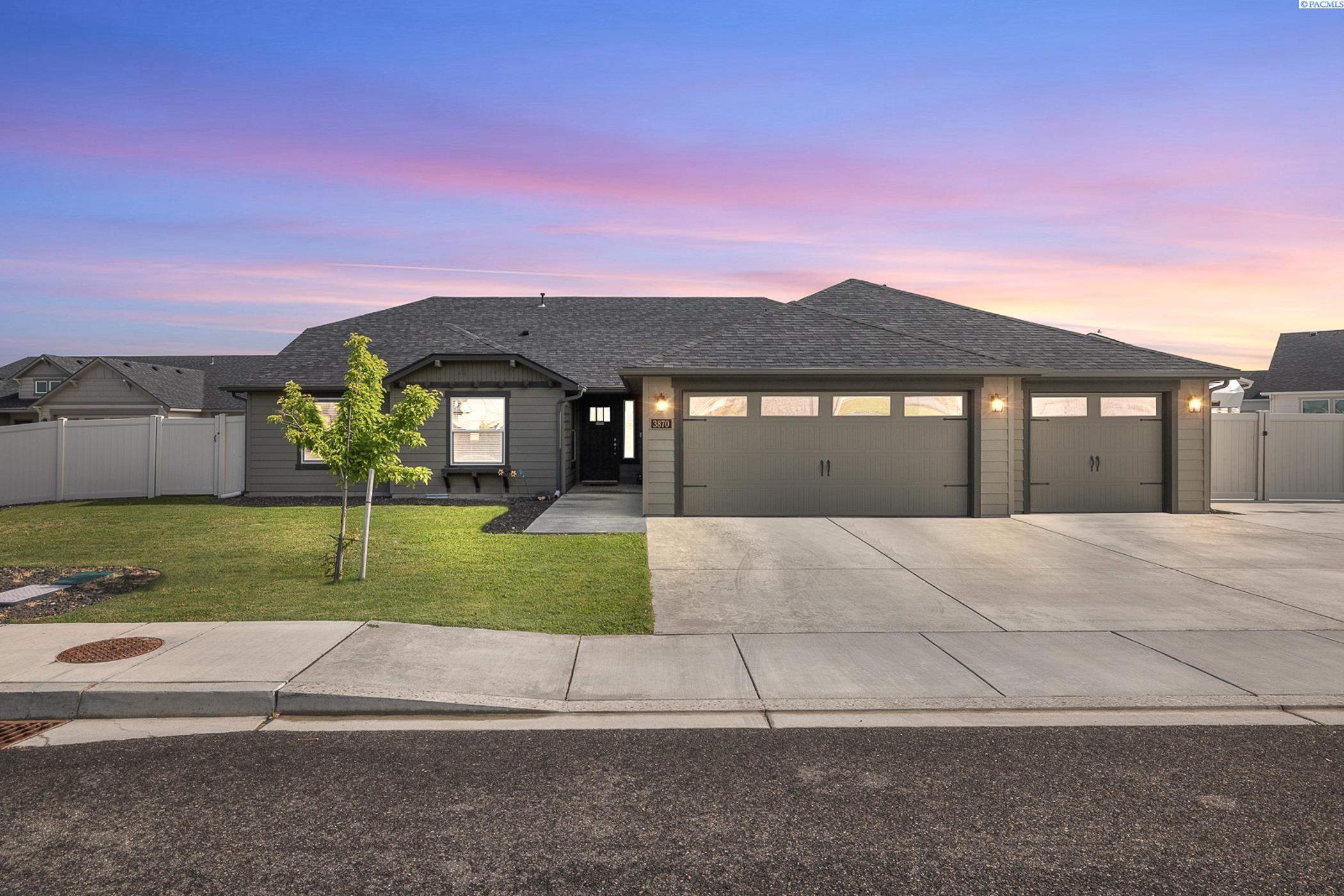 Gray single-story home with two garage doors, a broad driveway, and a fenced lawn at sunset.