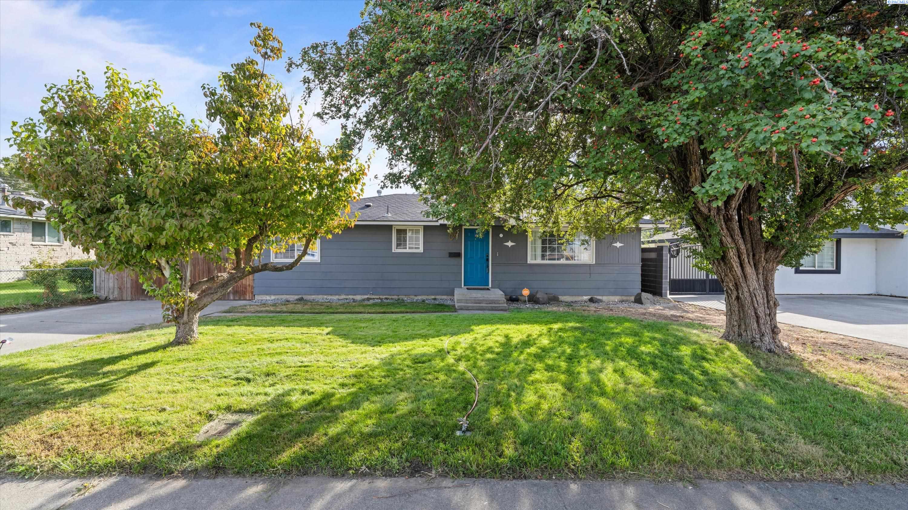 Gray single-story house with a bright blue front door, framed by mature trees and a green lawn.