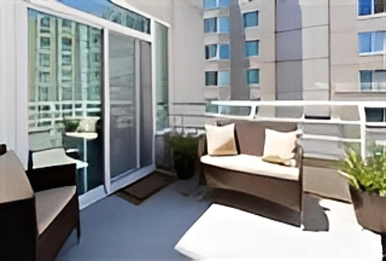 Apartment balcony with cushioned seating, potted plants, and views of neighboring buildings.