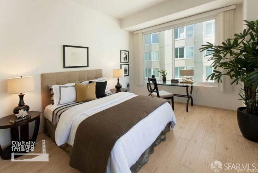 Bedroom with a large bed, desk, and wide windows overlooking a neighboring apartment building.