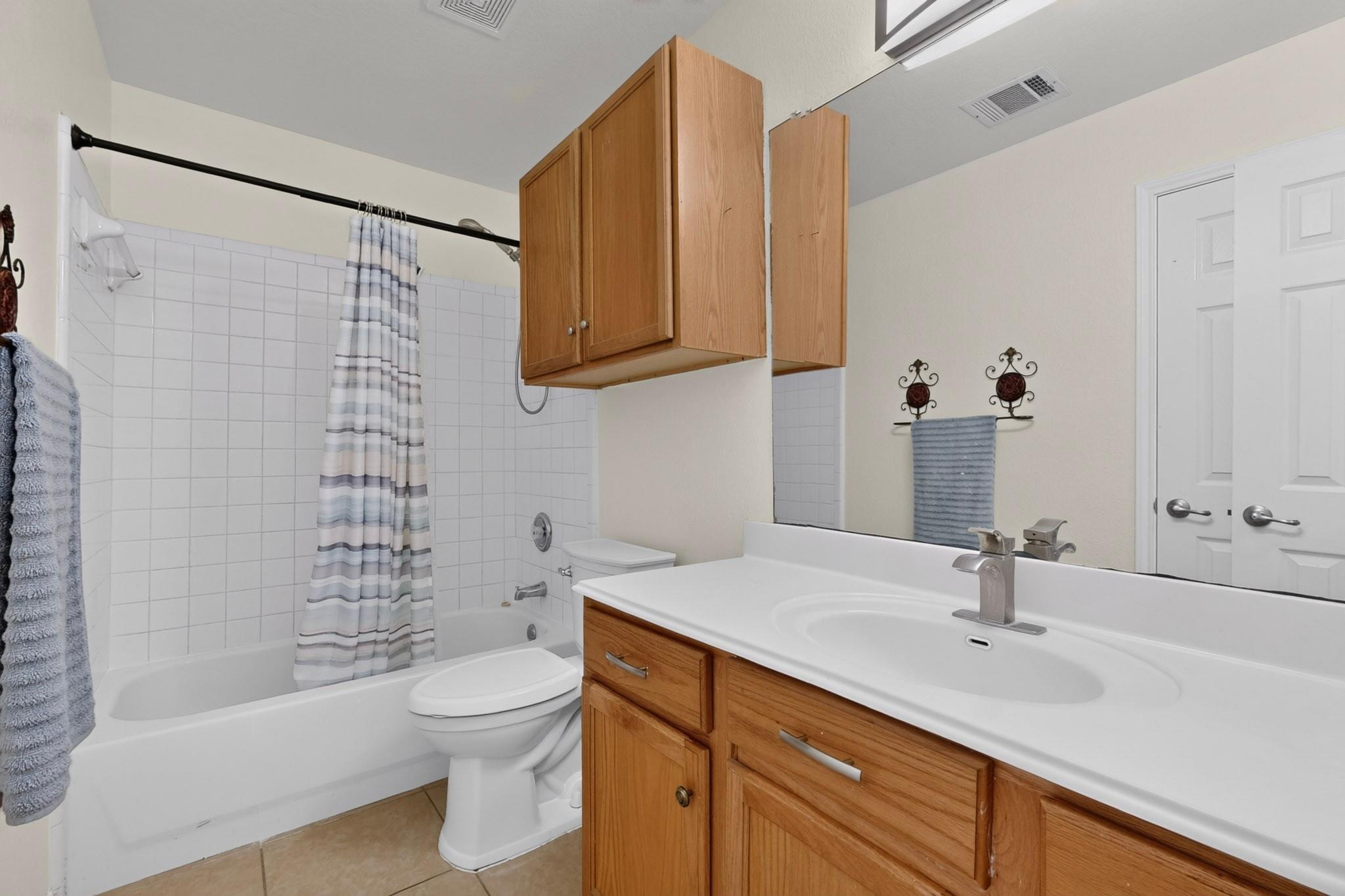 Bathroom with a tiled tub and shower, toilet, and wood vanity with overhead cabinets.