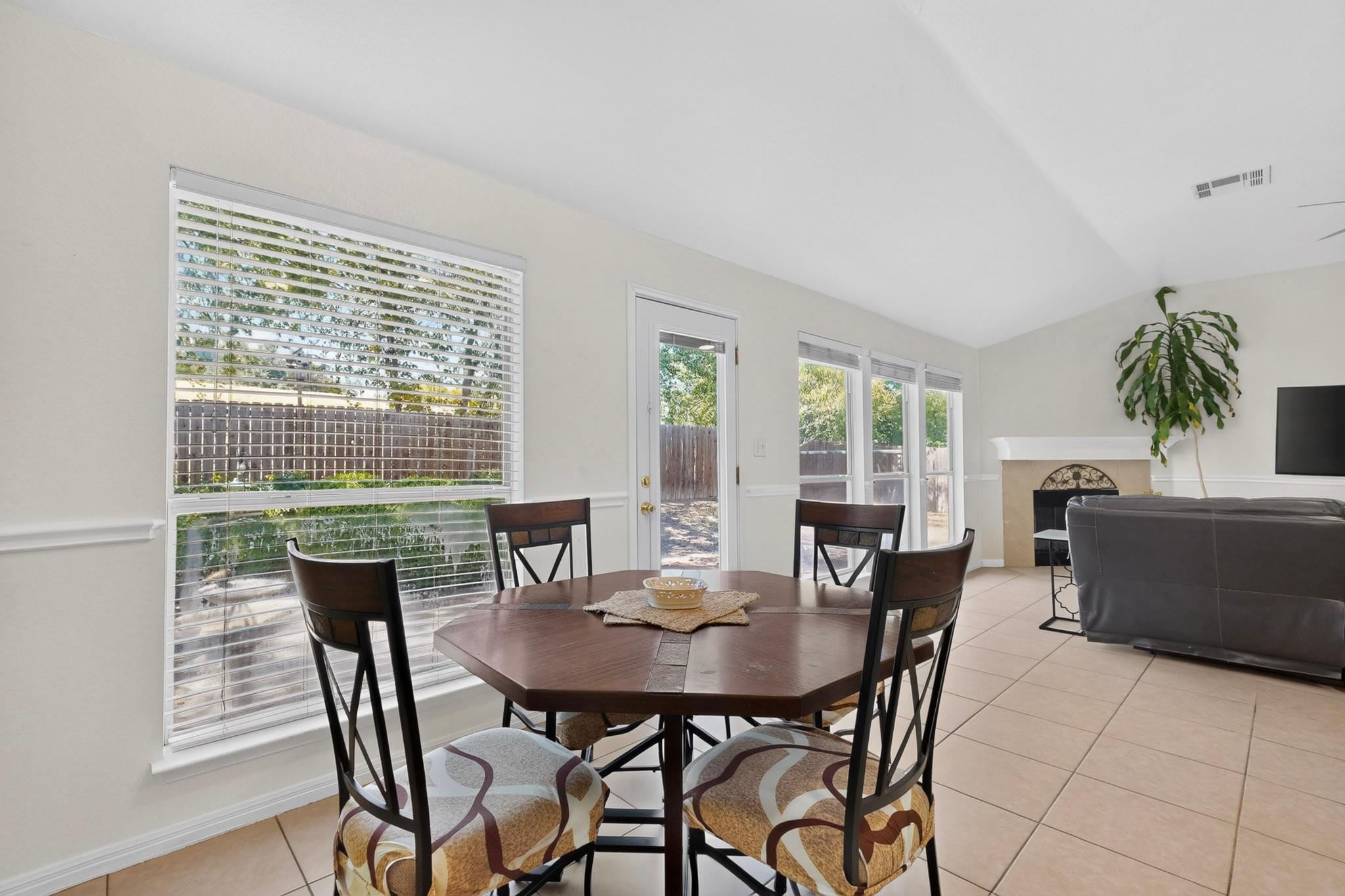 Dining area with a dark wood table beside large windows, opening into a living room with a fireplace.
