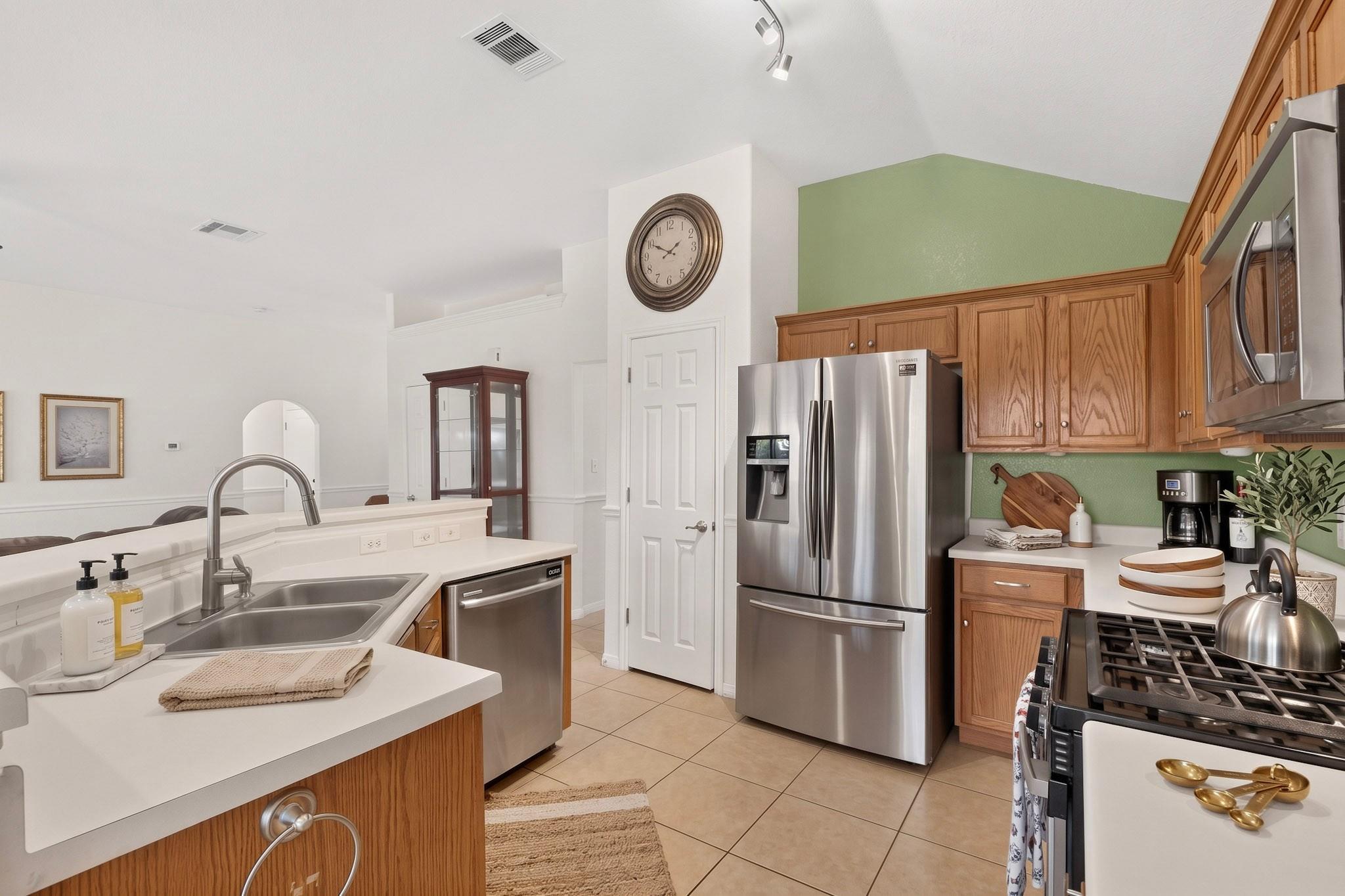 Kitchen with warm wood cabinets, green accent wall, stainless appliances, and a white island with double sink.