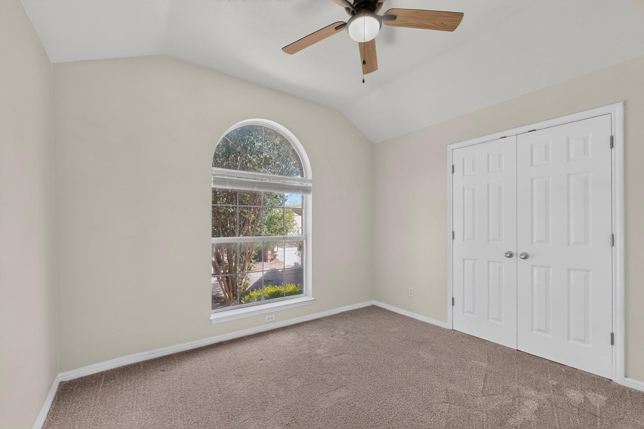 Empty bedroom with an arched window, beige carpet, and white double closet doors.