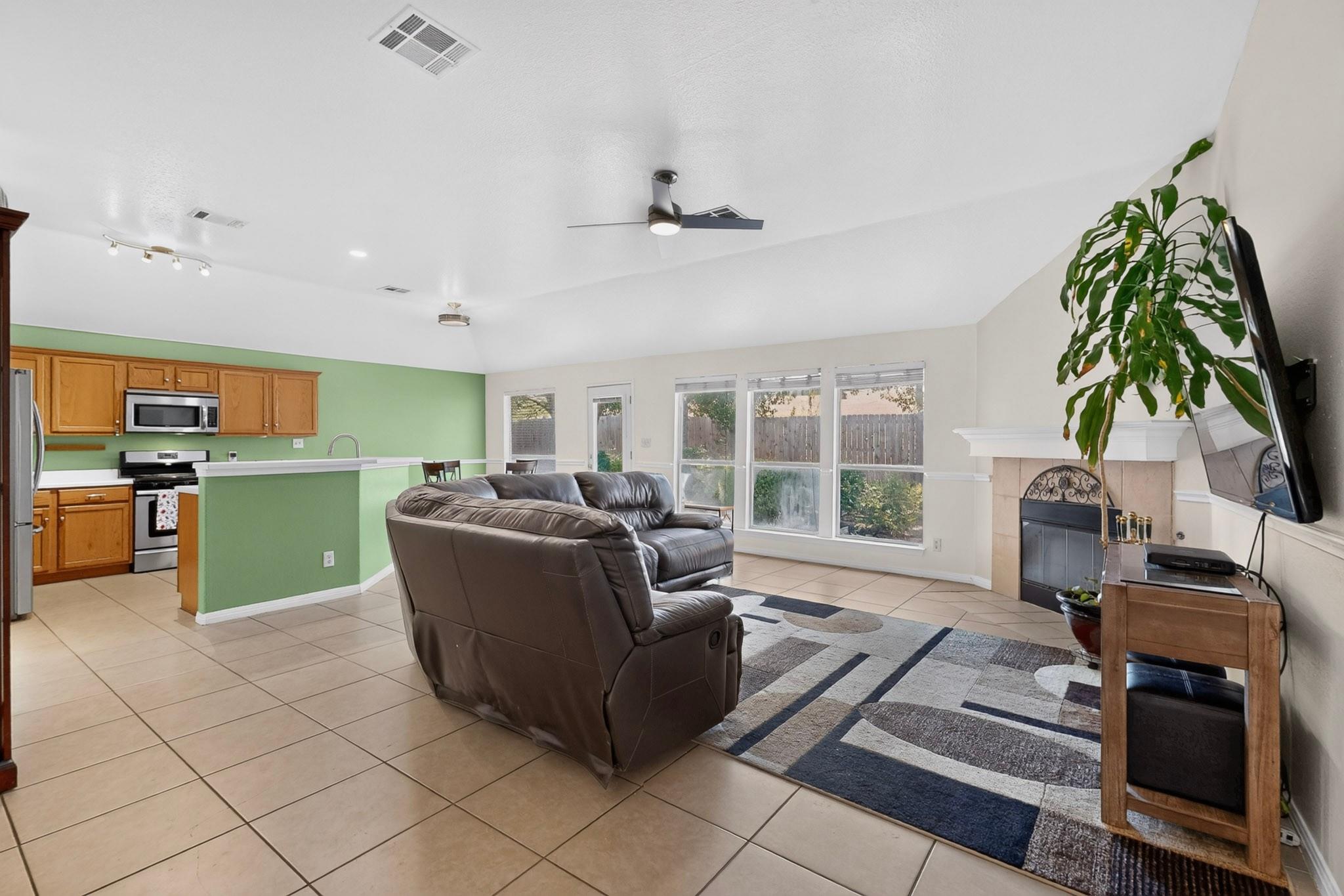 Living room with a leather sectional, fireplace, large windows, and an open kitchen with a green breakfast bar.