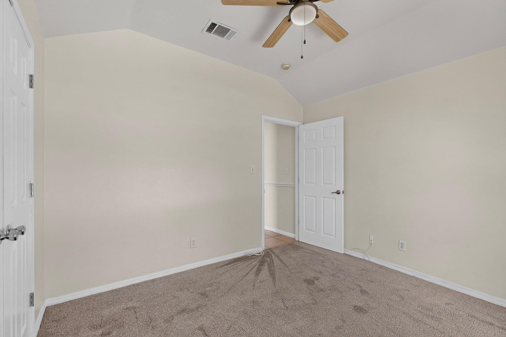 Empty bedroom with beige carpet, a vaulted ceiling, and a wood-blade ceiling fan.