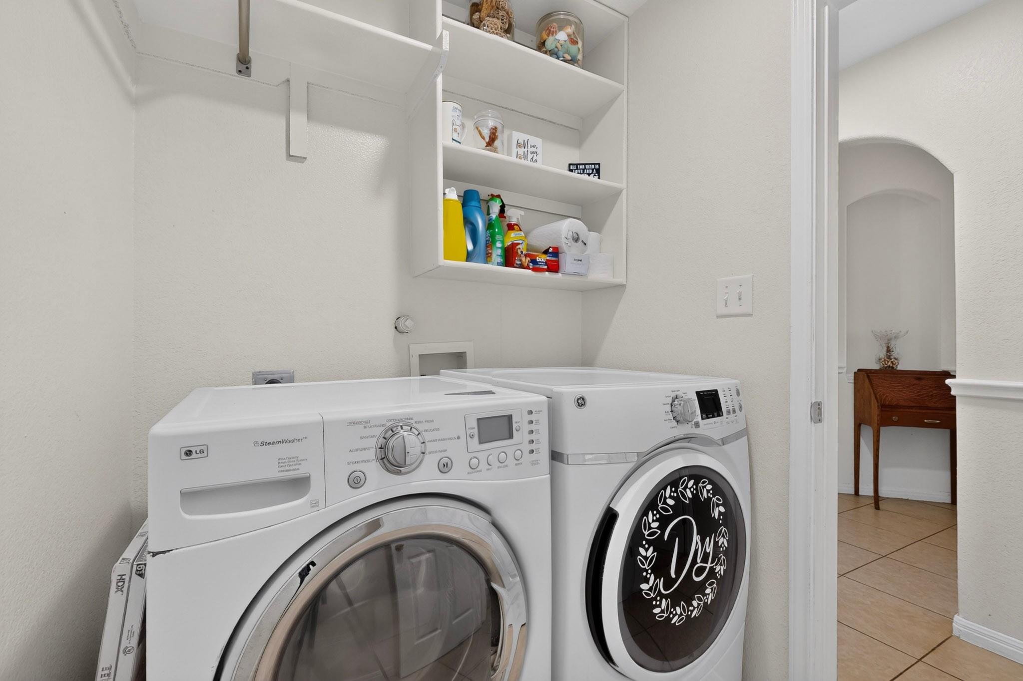 Laundry room with front-loading washer and dryer beneath shelves stocked with cleaning supplies.