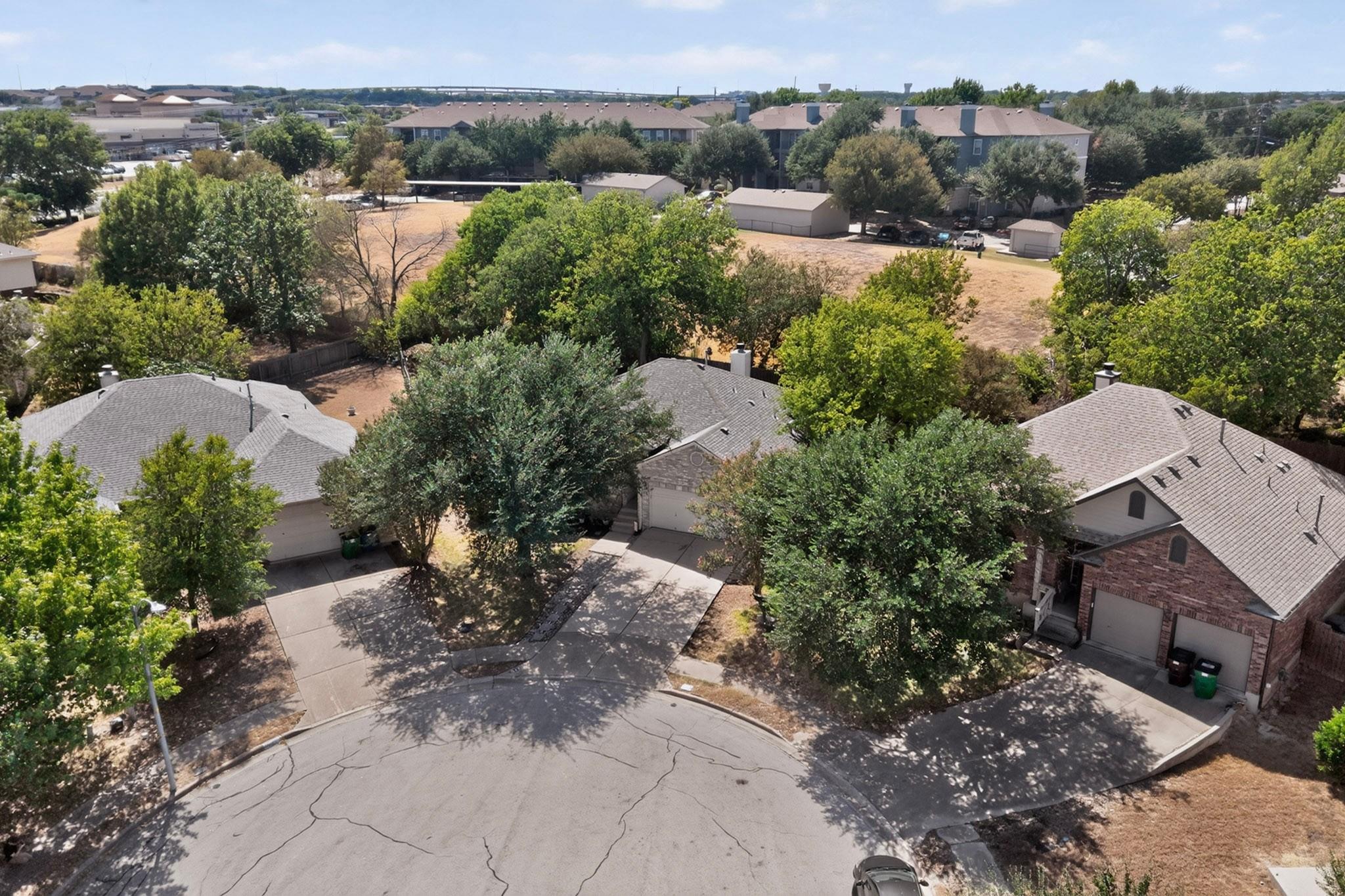 Aerial view of homes along a tree-shaded cul-de-sac, with apartment buildings in the background.