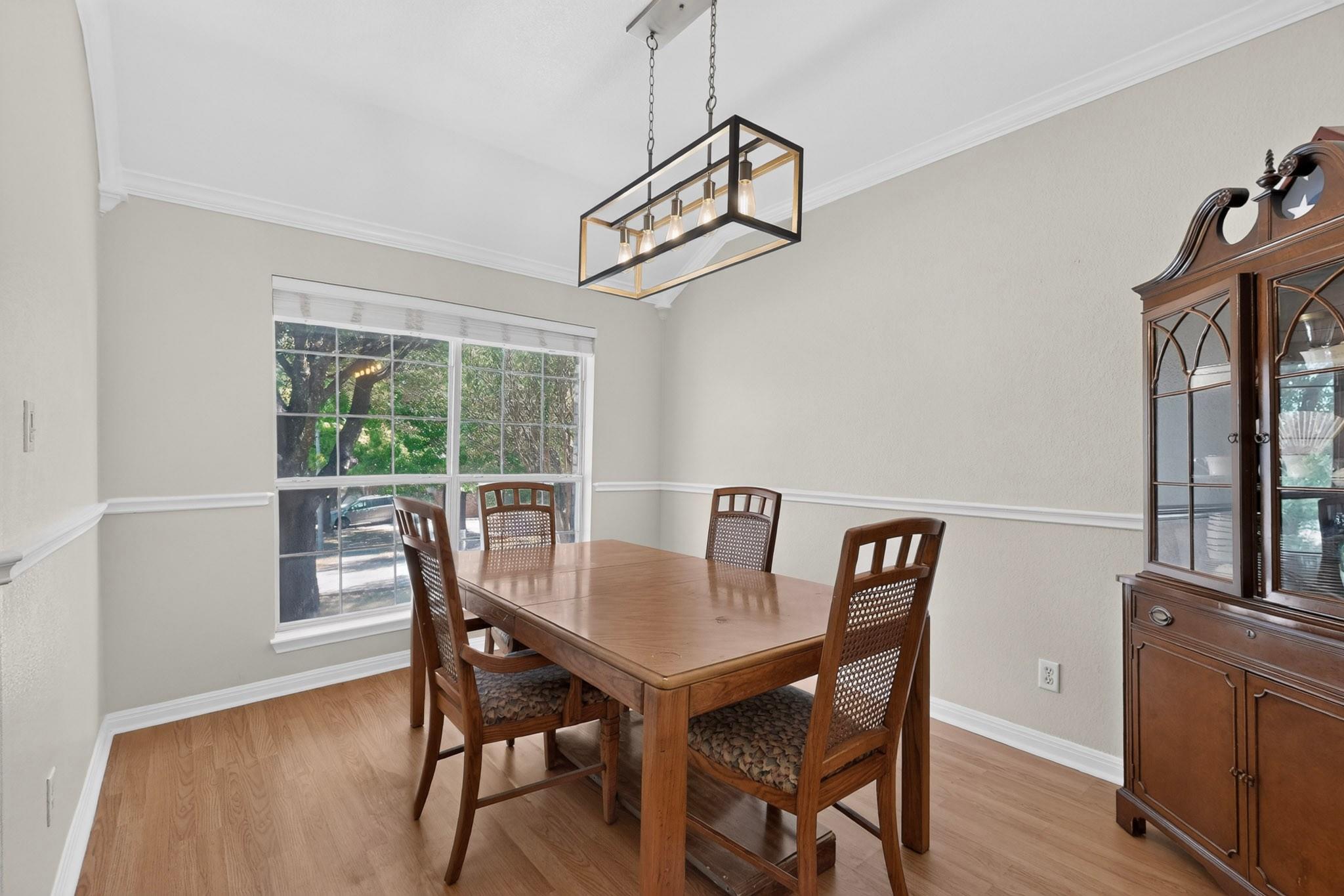 Dining room with a wooden table, woven-seat chairs, large window, and glass-front china cabinet.