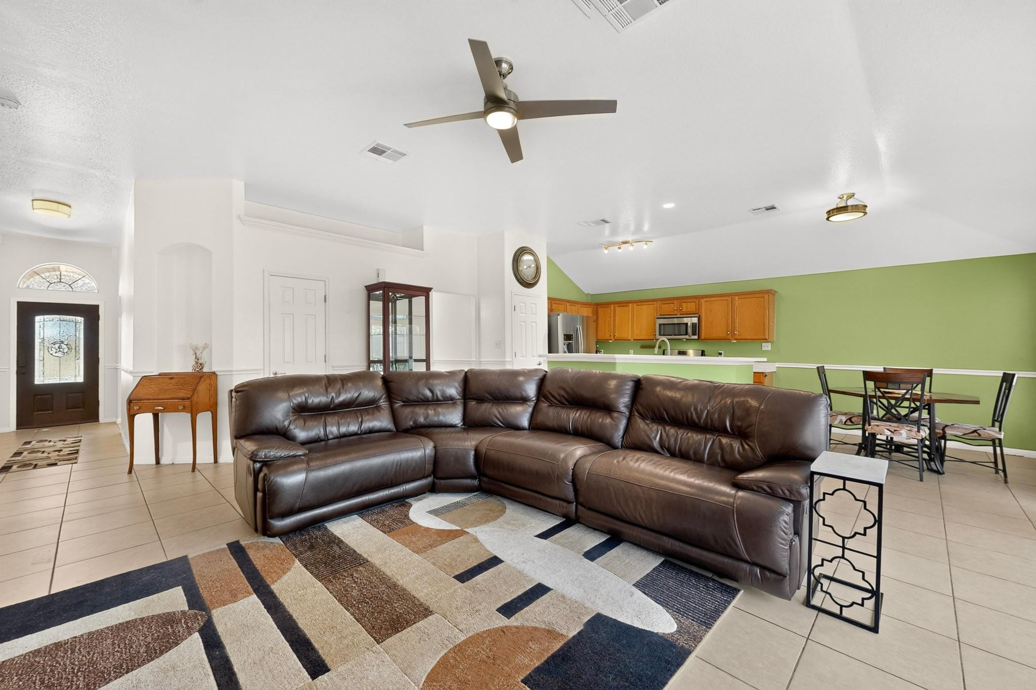 Open-plan living room with a dark leather sectional, geometric rug, dining area, and green-walled kitchen.
