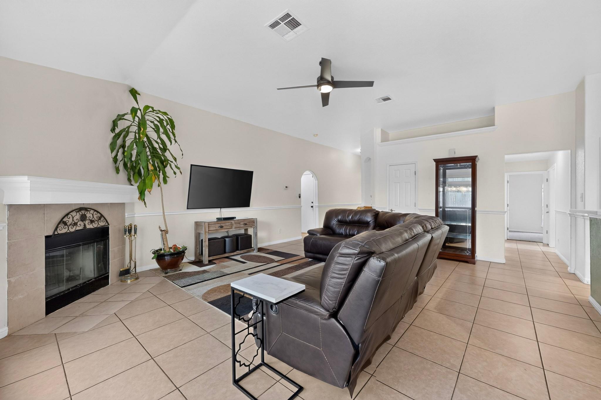 Living room with a tiled floor, stone fireplace, and dark leather sectional sofa.